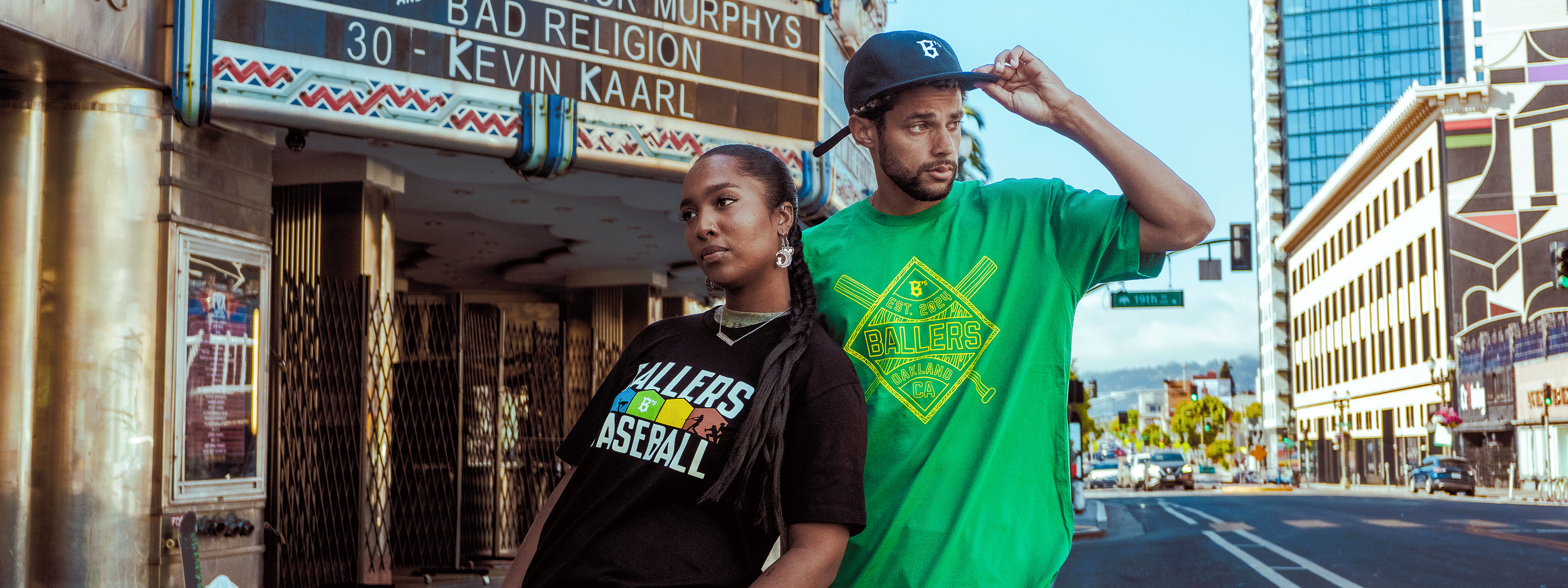 Two people wearing casual streetwear with "B's VALLEY" logos. One leans against a green counter, the other crouches. In the background, hats and shirts are displayed on shelves. The scene appears relaxed and urban.