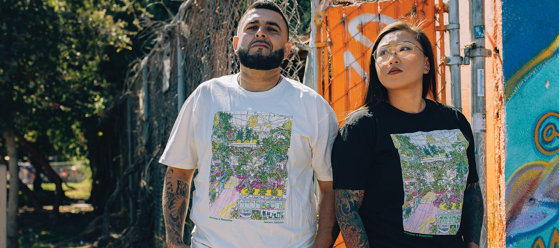 Models wearing natural and black tees of our Planterday collab design, large front print depicting the shop, models posing outdoors.