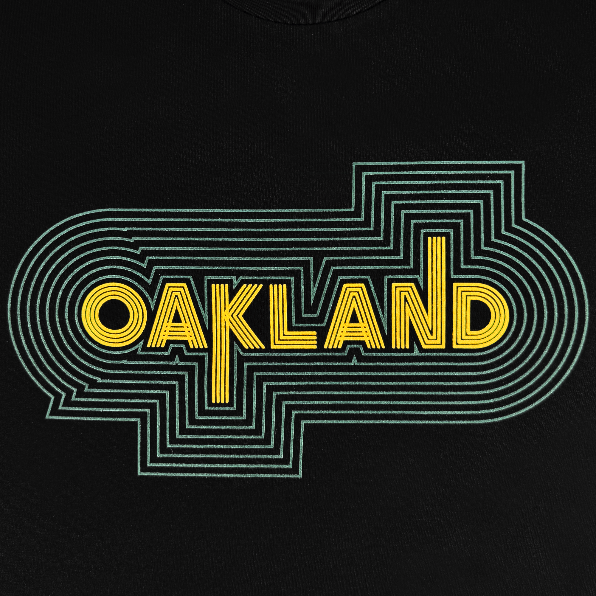 The image showcases an Oaklandish graphic featuring bold, yellow geometric "OAKLAND" text and multiple green concentric lines for a layered, retro sports vibe on the sleek black Oakland Sports Culture '68 Tee.