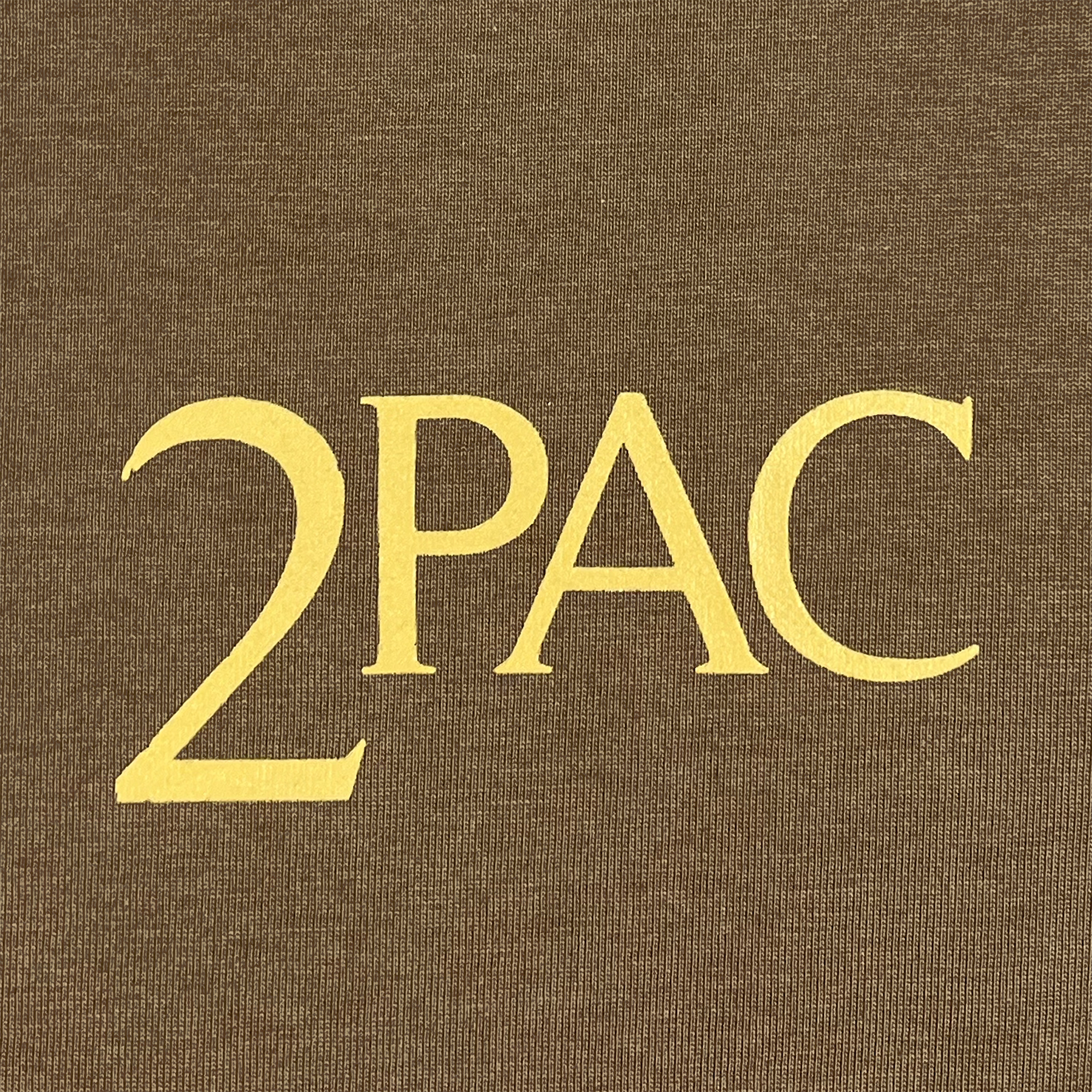 The Against the World Tee from Oaklandish showcases "2PAC" in prominent, bold yellow letters set against a brown background. The classic serif font captures the timeless essence of Tupac Shakur's iconic hip-hop style.