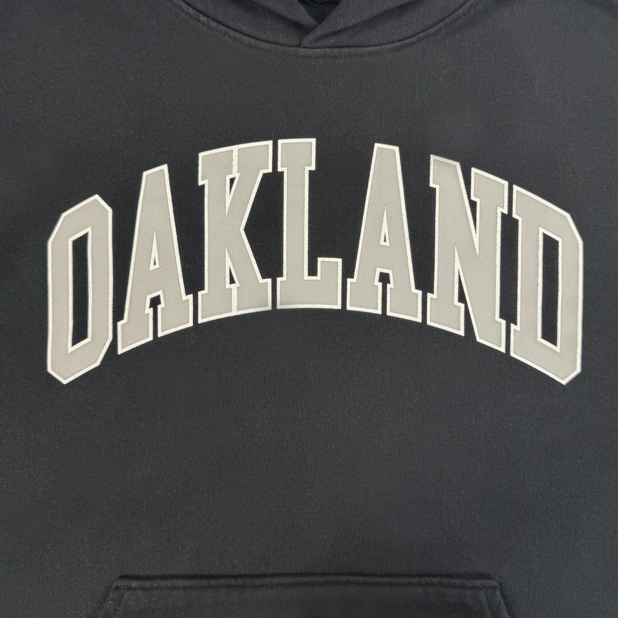 The Oaklandish Alma Mater Hoodie 2.0 is a black men’s pullover featuring "OAKLAND" in bold, white arched letters with a shadow effect across the chest, designed in an oversized fleece style for maximum comfort.