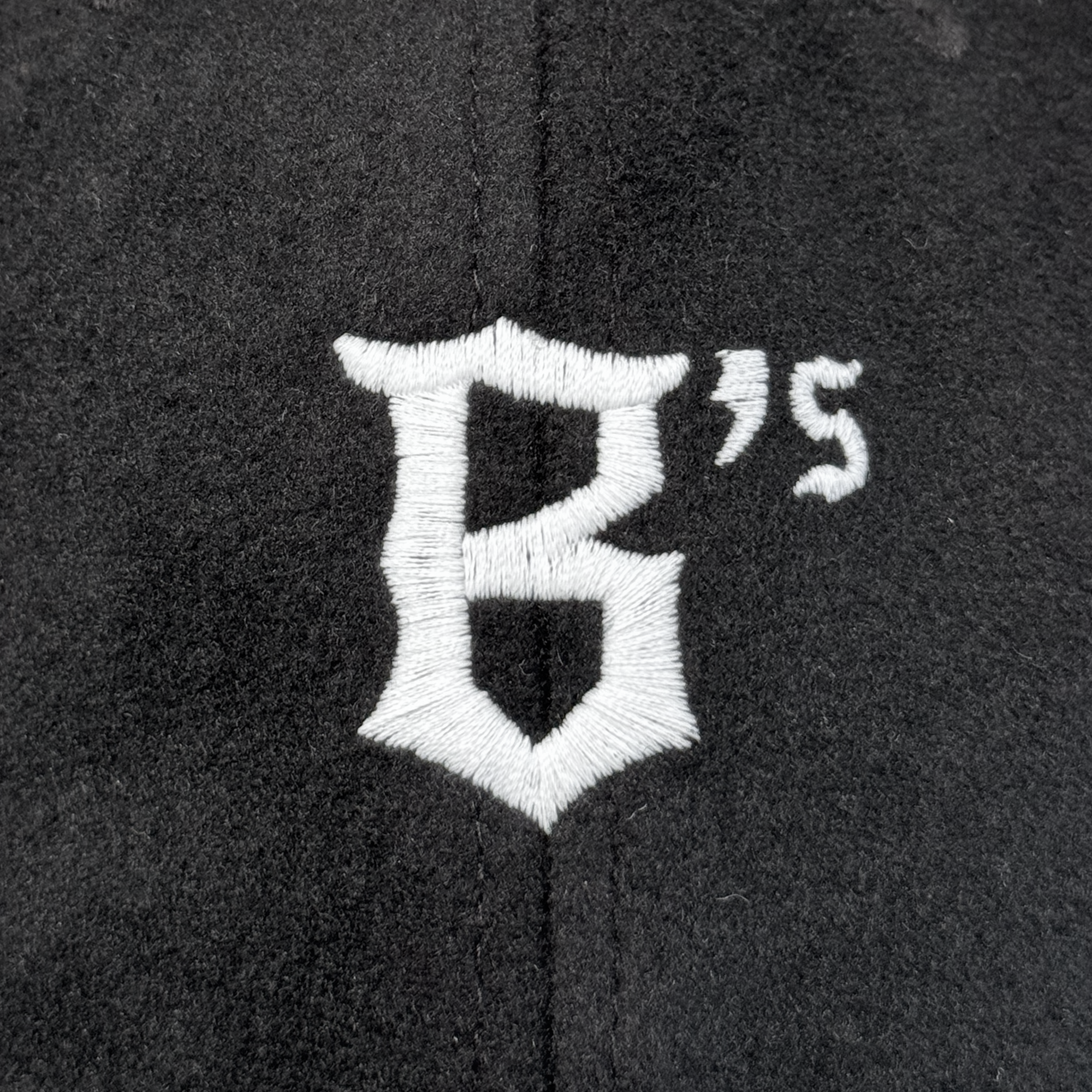 The Oakland Ballers B Strapback by Oakland Ballers features a white embroidered "B" with a shield outline and small "’S" at the upper right on black fabric, plus a vertical seam down the center, reflecting its adjustable strapback hat design.