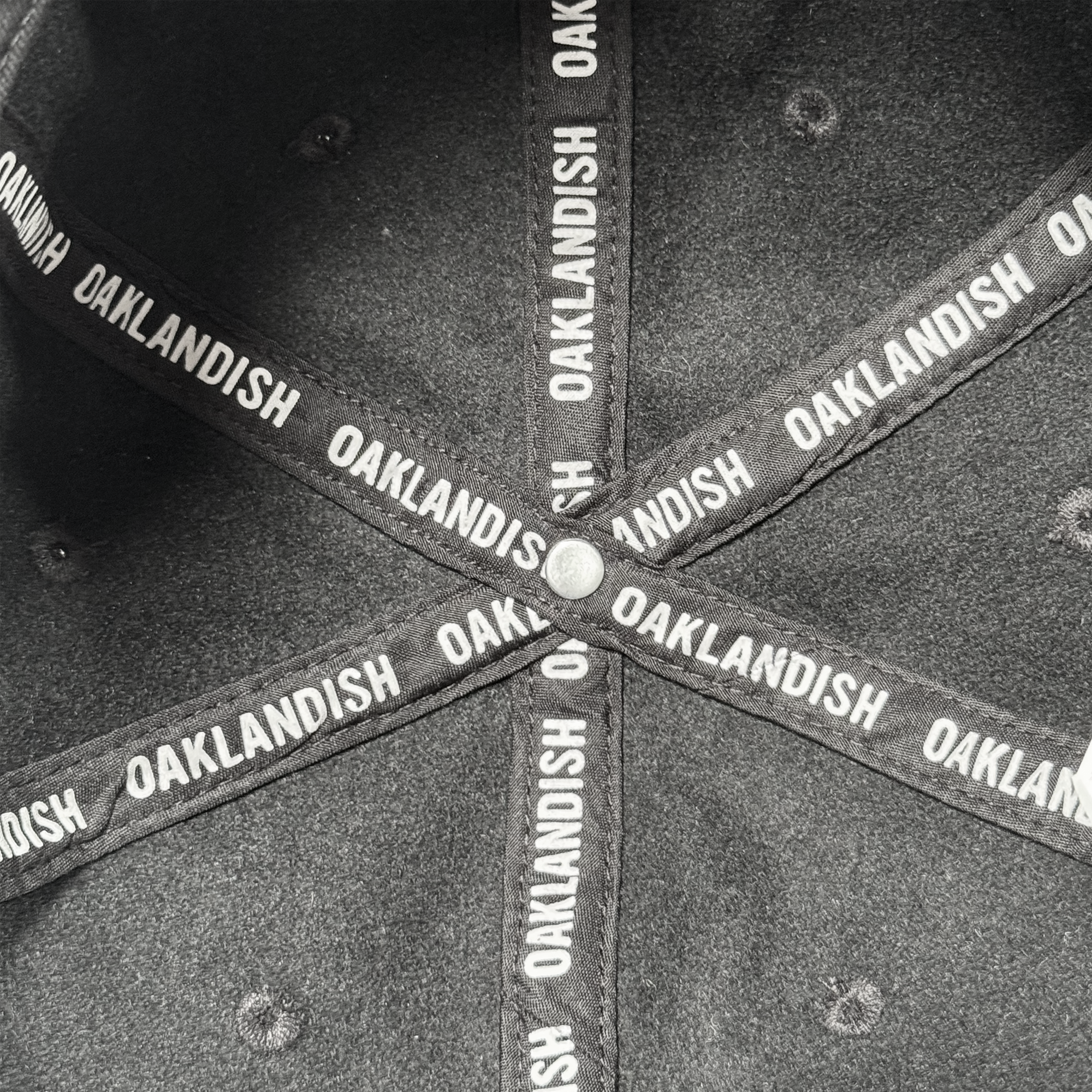 Close-up of the inside of an Oakland Ballers B Strapback hat, showing crossed black fabric strips with “OAKLANDISH” in white uppercase letters and a metal button at the intersection. Brand: Oakland Ballers.