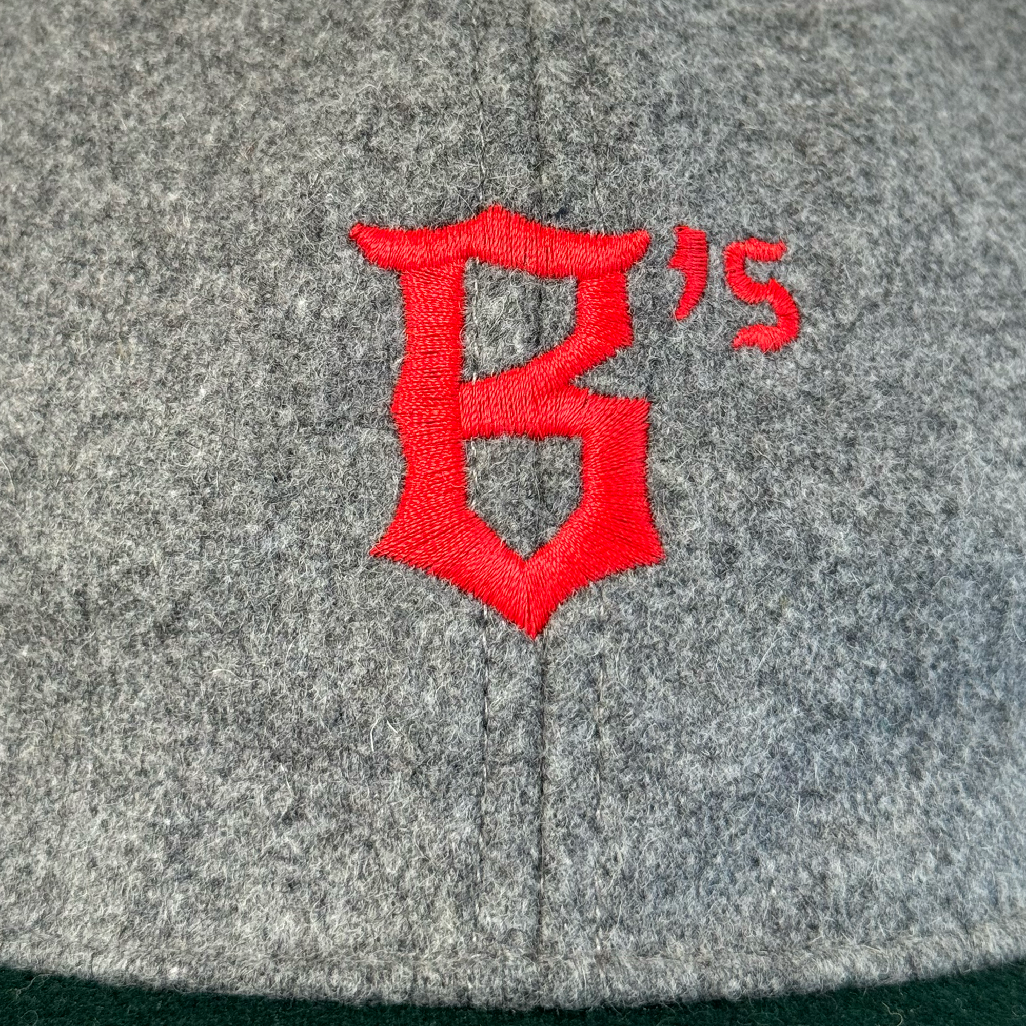 A close-up of the Oakland Ballers B Strapback by Oakland Ballers shows its gray polyester wool fabric, detailed stitching, and bold red embroidered B logo with a small raised “’s.” The texture and craftsmanship stand out.