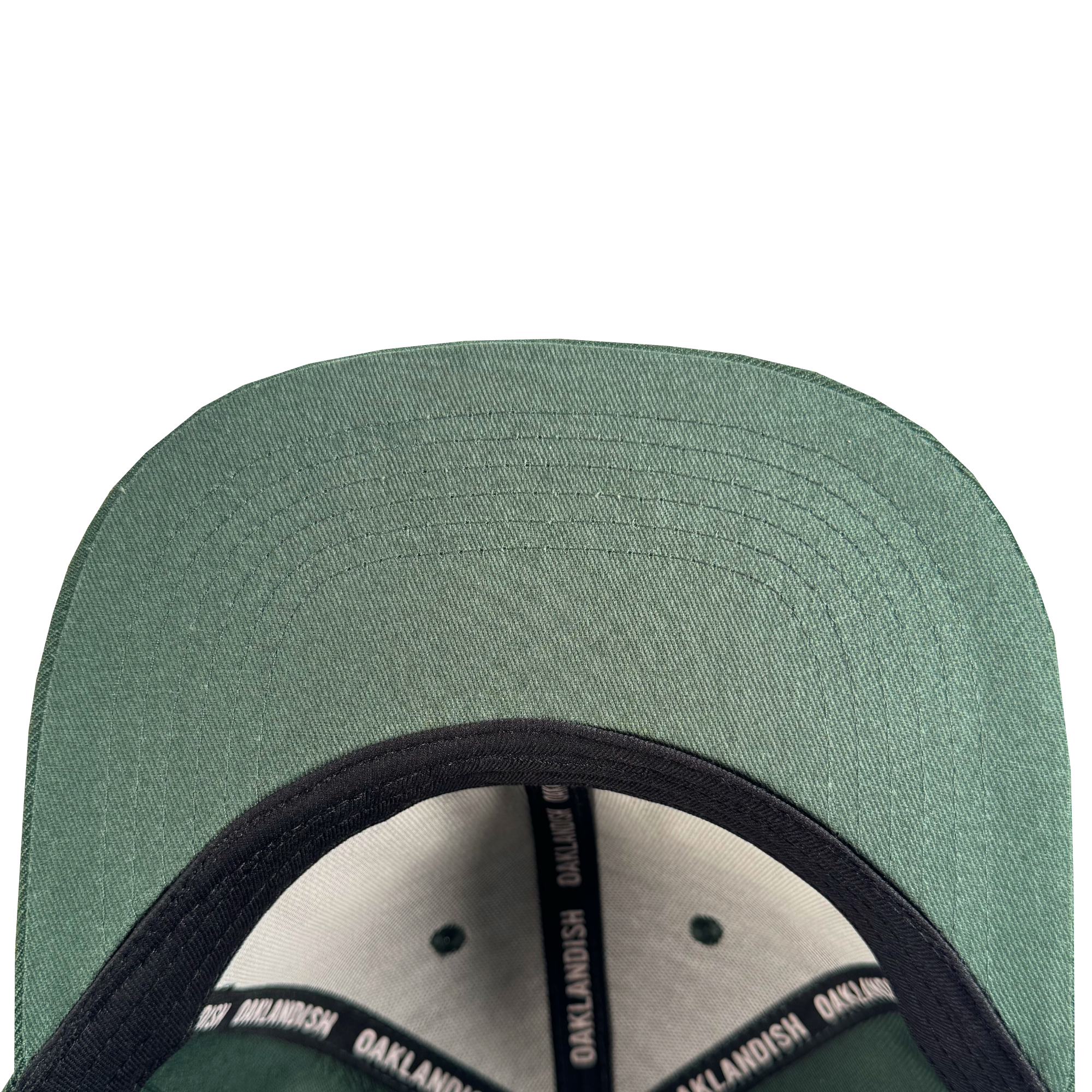 Close-up of the Oakland Ballers Flexfit Cap: a green baseball hat with a black inner lining and sweatband featuring repeated “OAKLANDISH” text, celebrating Oakland Ballers pride. Detailed stitching accents the underside of the brim.