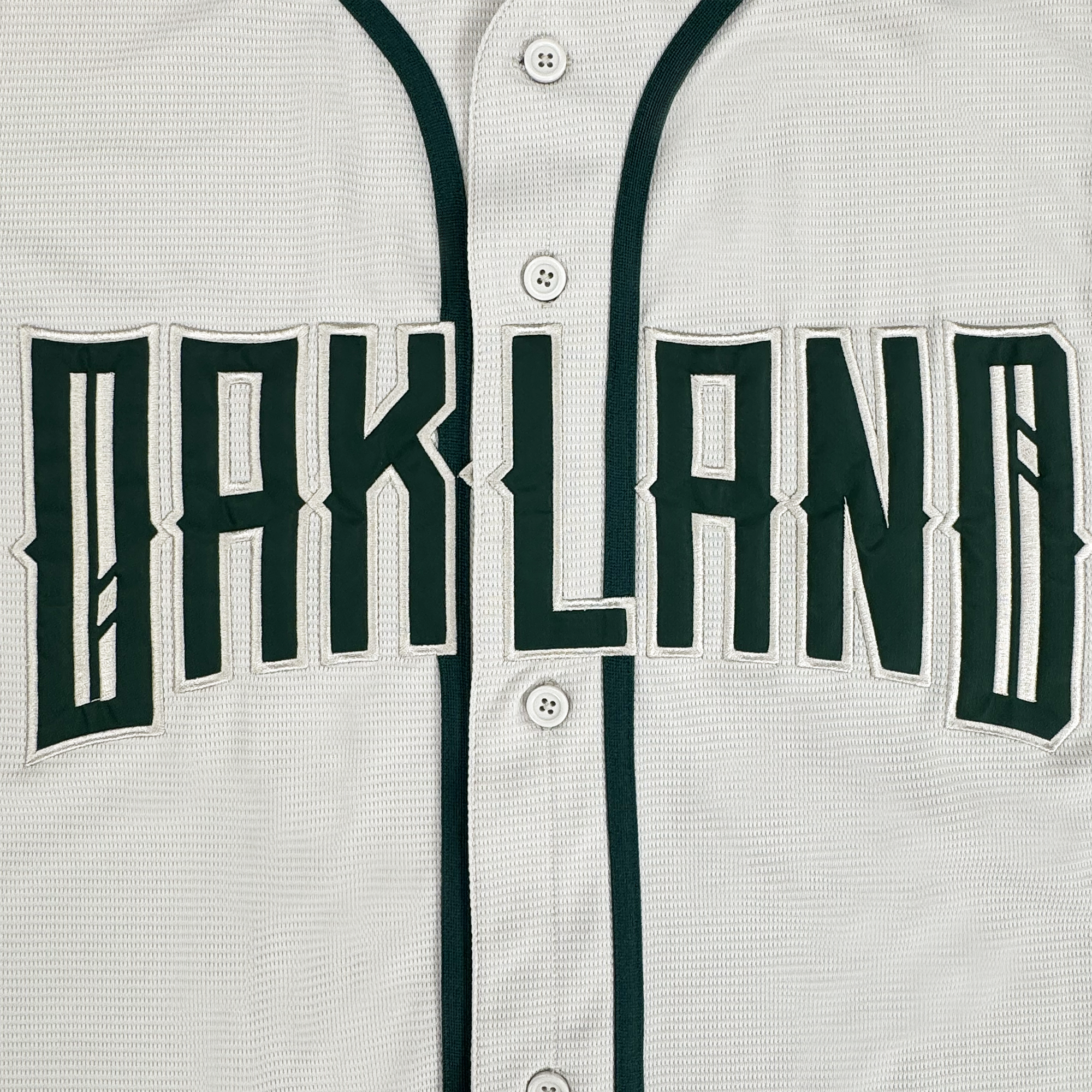 A close-up of the Oakland Ballers Button Up Jersey, featuring white fabric with dark green trim and buttons. “OAKLAND” is boldly displayed across the chest, representing the Oakland Ballers brand.