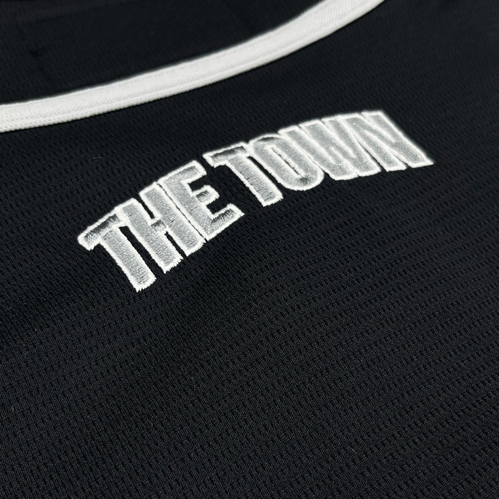 Close-up of black mesh fabric from the Oakland Ballers Button Up Jersey by Oakland Ballers, featuring bold raised white embroidery spelling “THE TOWN” and accented with white trim—a tribute to the Pioneer League's newest team.