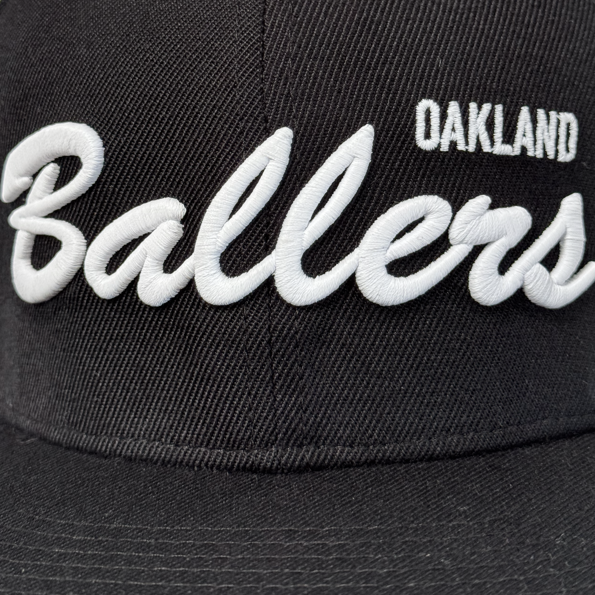 Close-up of the Oakland Ballers Script Snapback by Oakland Ballers, a black adjustable hat with "OAKLAND" in white block letters above a large embroidered Ballers script. Fabric texture and stitching are clearly shown.