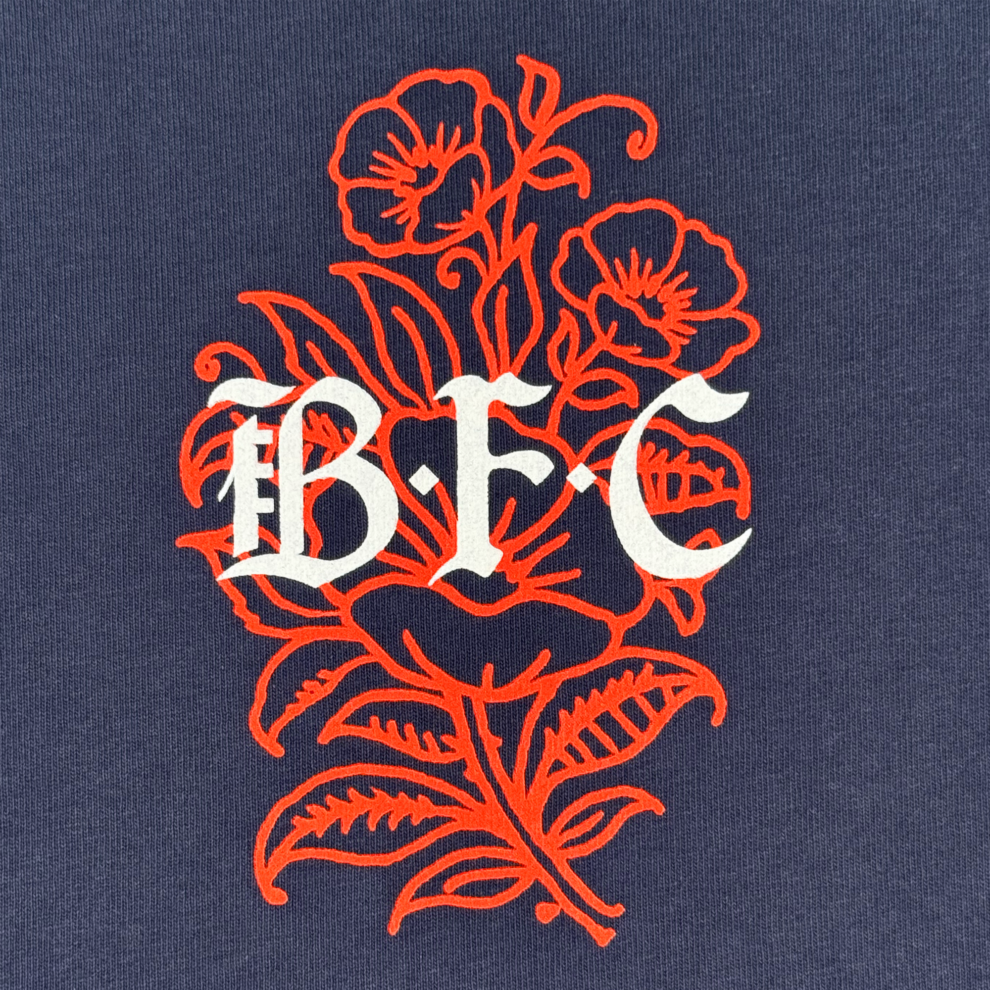 The Bay FC Flora Tee features ornate red floral line art on a dark blue background with bold white Gothic "BFC" lettering, reflecting Bay FC's classic fit heavy-weight cotton style.
