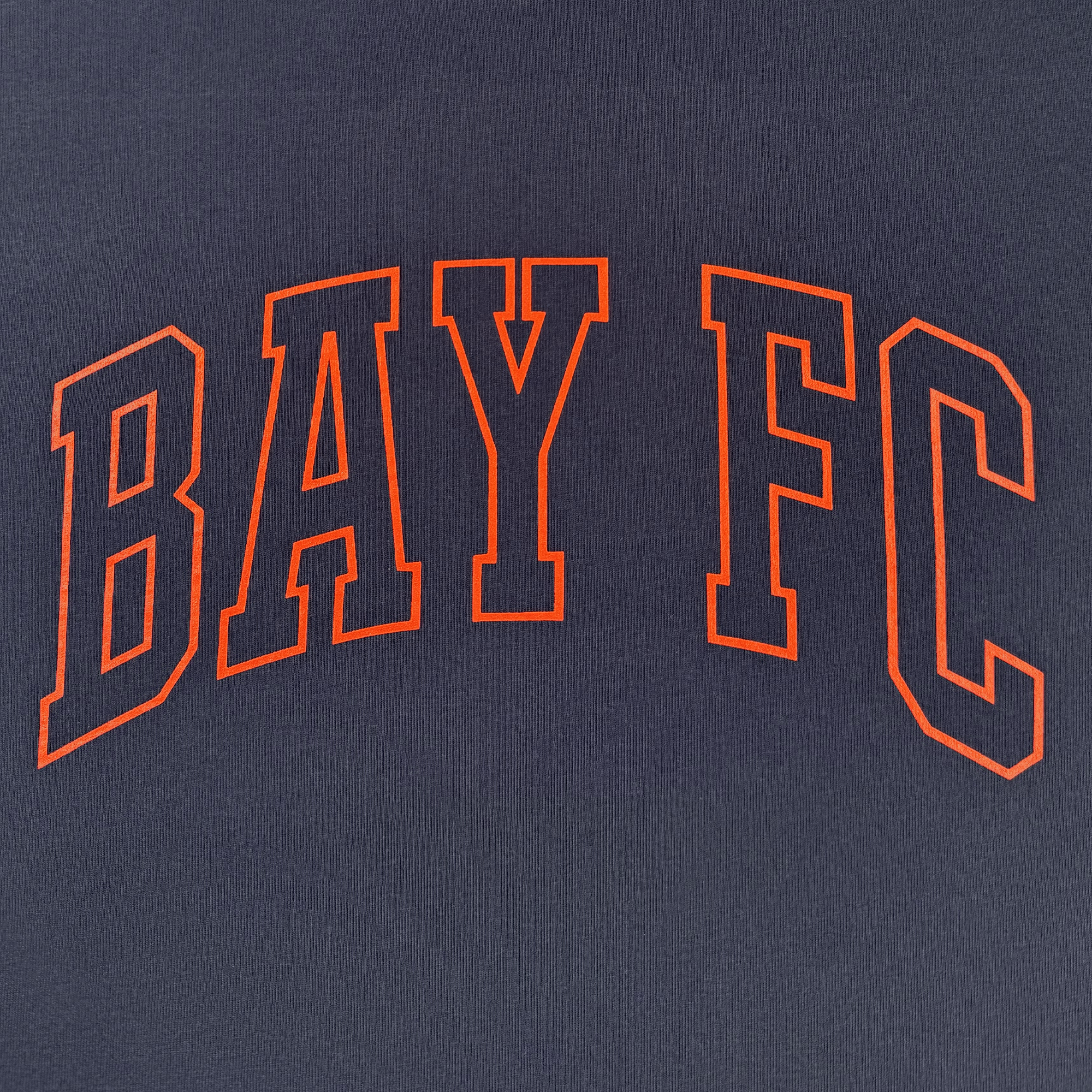 Close-up of "BAY FC" in bold, outlined orange font arched over dark blue ribbed heavy-weight cotton on the Bay FC Varsity Tee—perfect for a classic fit t-shirt by Bay FC.