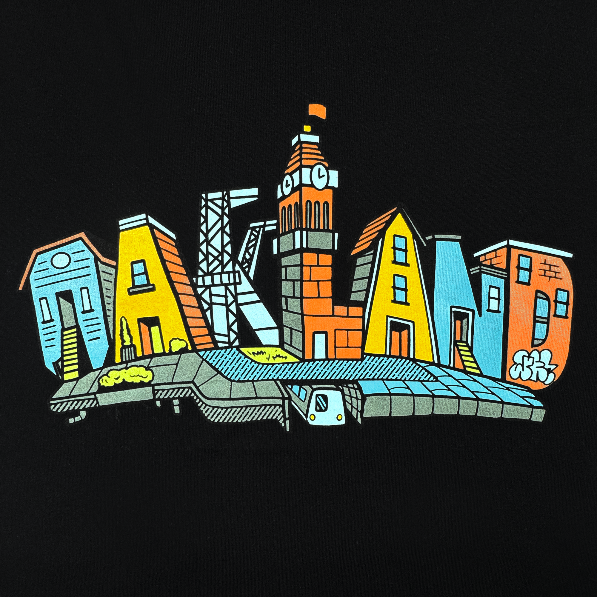 The Oaklandish Youth Blockletters Tee features “Oakland” in vibrant building-style letters inspired by the skyline. The “L” is a clock tower, with a BART train, greenery, and graffiti details on a solid black kids cotton shirt.