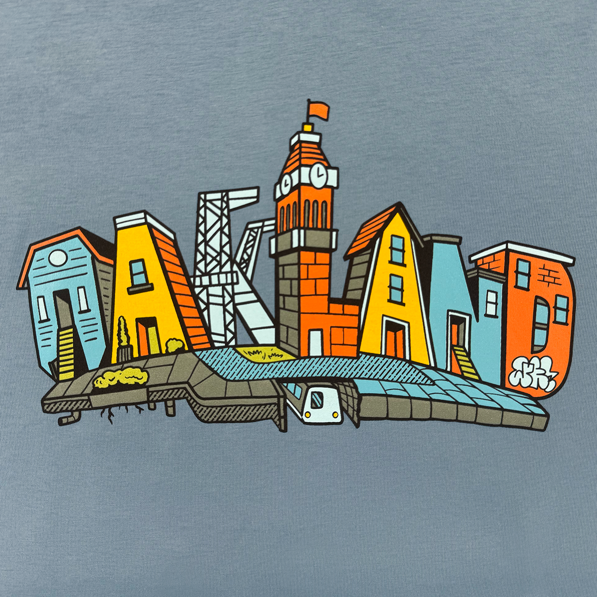 The Oaklandish Women's Blockletters Tee features "Oakland" spelled in illustrated, colorful buildings and landmarks—a clock tower as the "L" and an underground train—capturing the urban skyline on soft cotton.
