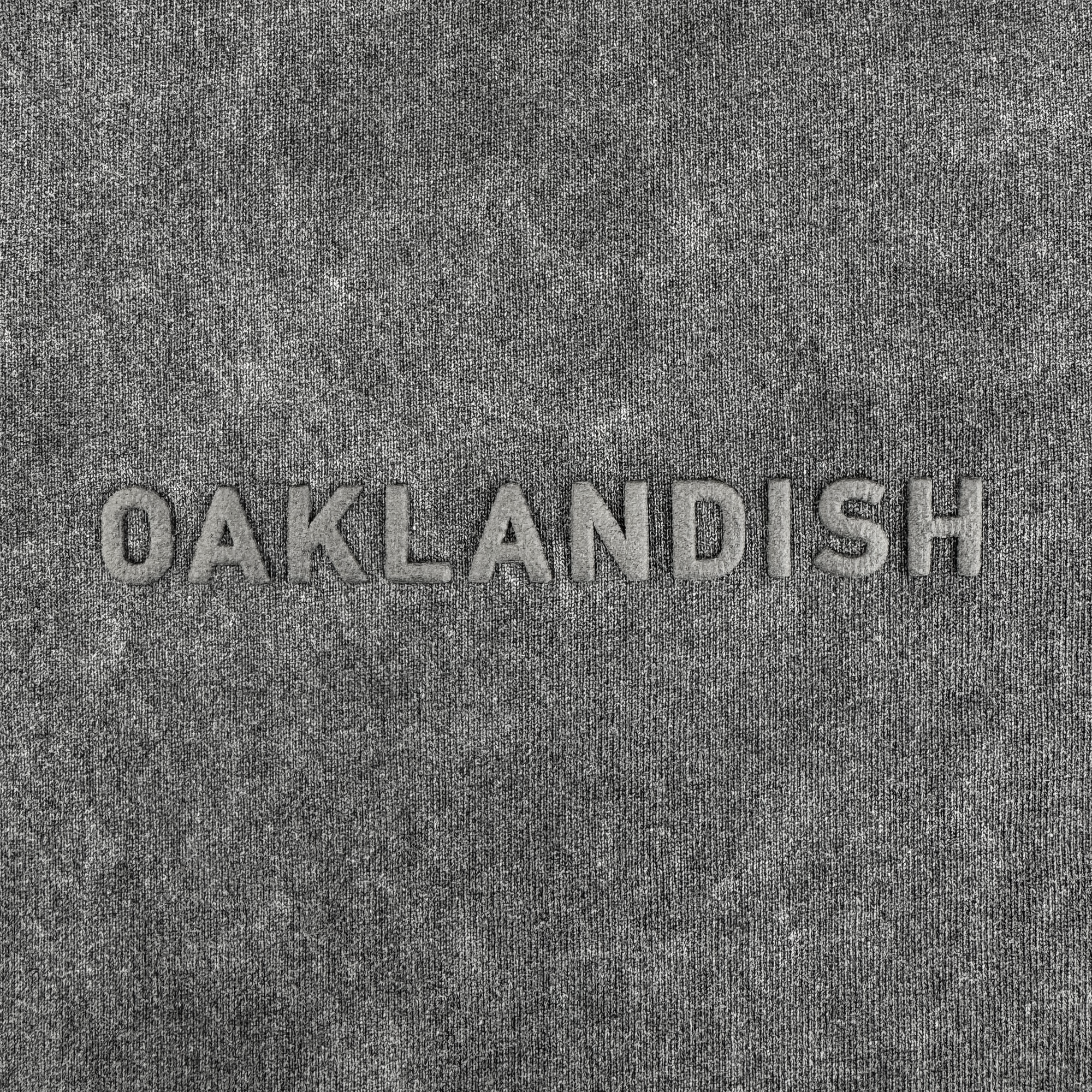 The Oaklandish Classic Logo Tee by Oaklandish features heavyweight gray textured cotton and bold raised “OAKLANDISH” embroidery in a lighter gray centered across the faded black, oversized shirt for subtle contrast.