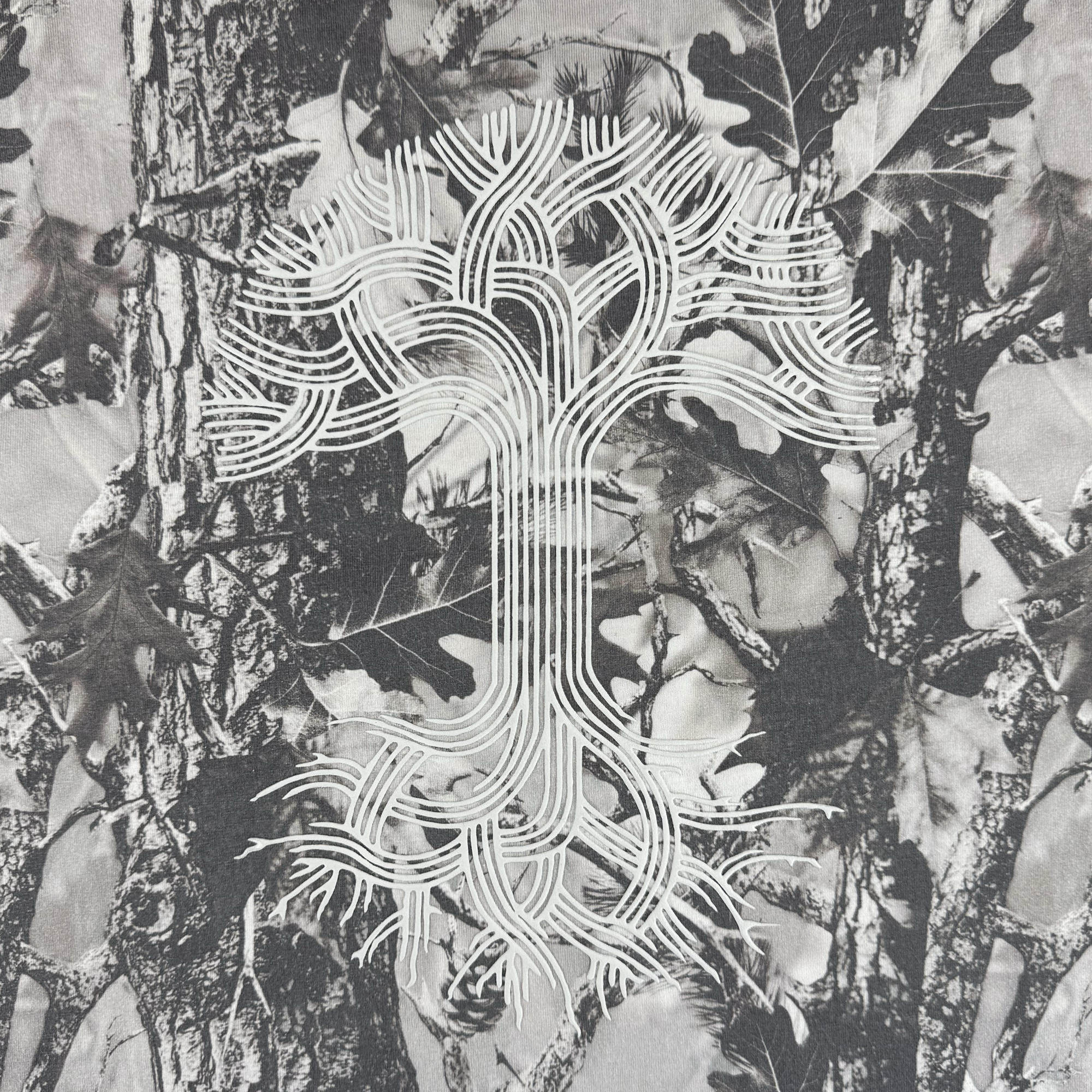 A black-and-white tree trunk and leaf background with a white, circuit-inspired tree logo is centered on the Oaklandish Classic Logo Tee by Oaklandish, blending nature and digital design on a heavyweight cotton oversized t-shirt.