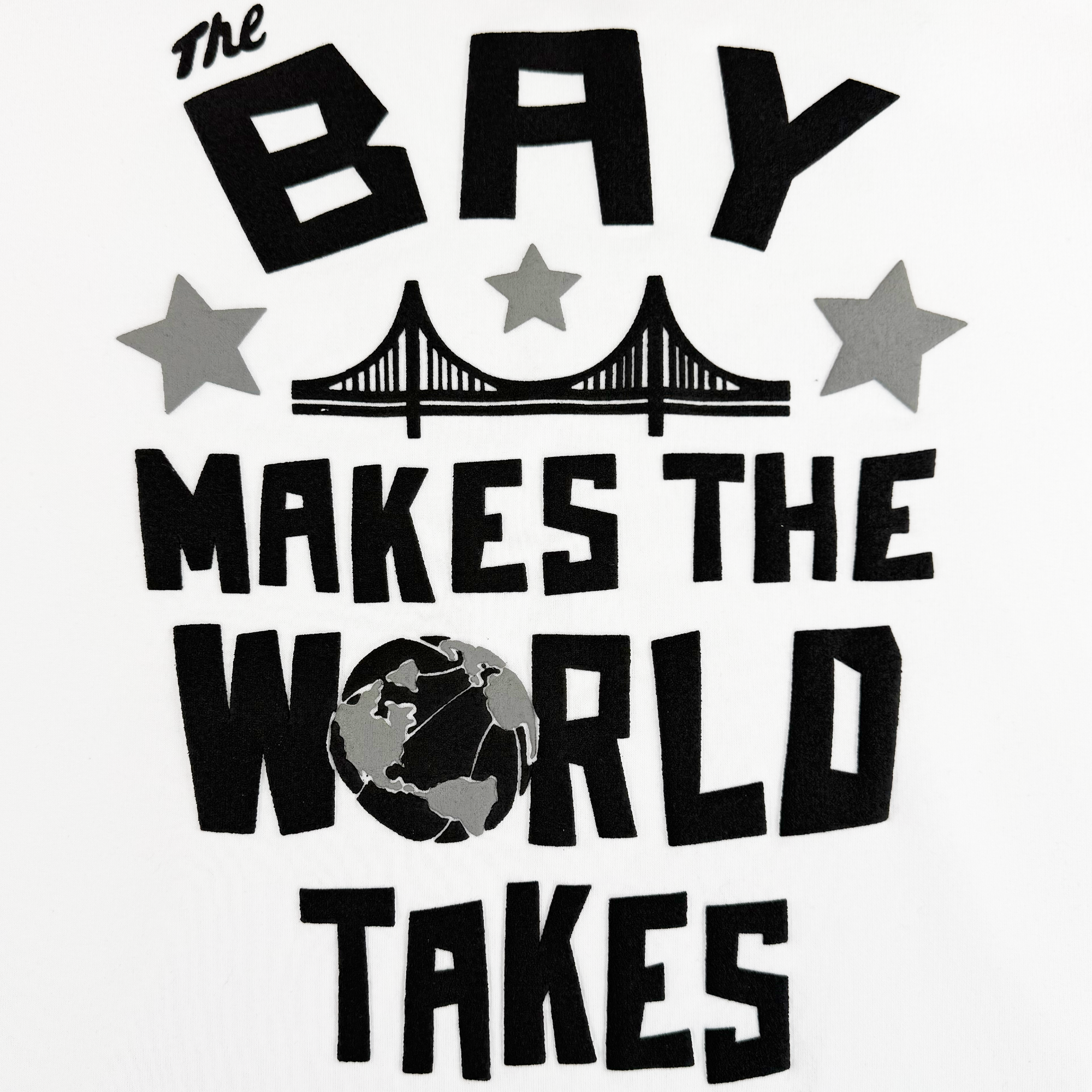 Black text on white reads, "The Bay Makes the World Takes," with a bridge and gray stars above. "WORLD" features a globe for the "O." Part of The Bay Collection, this Oaklandish Bay Bridge Hoodie By DOC V2 is a men's fleece pullover.