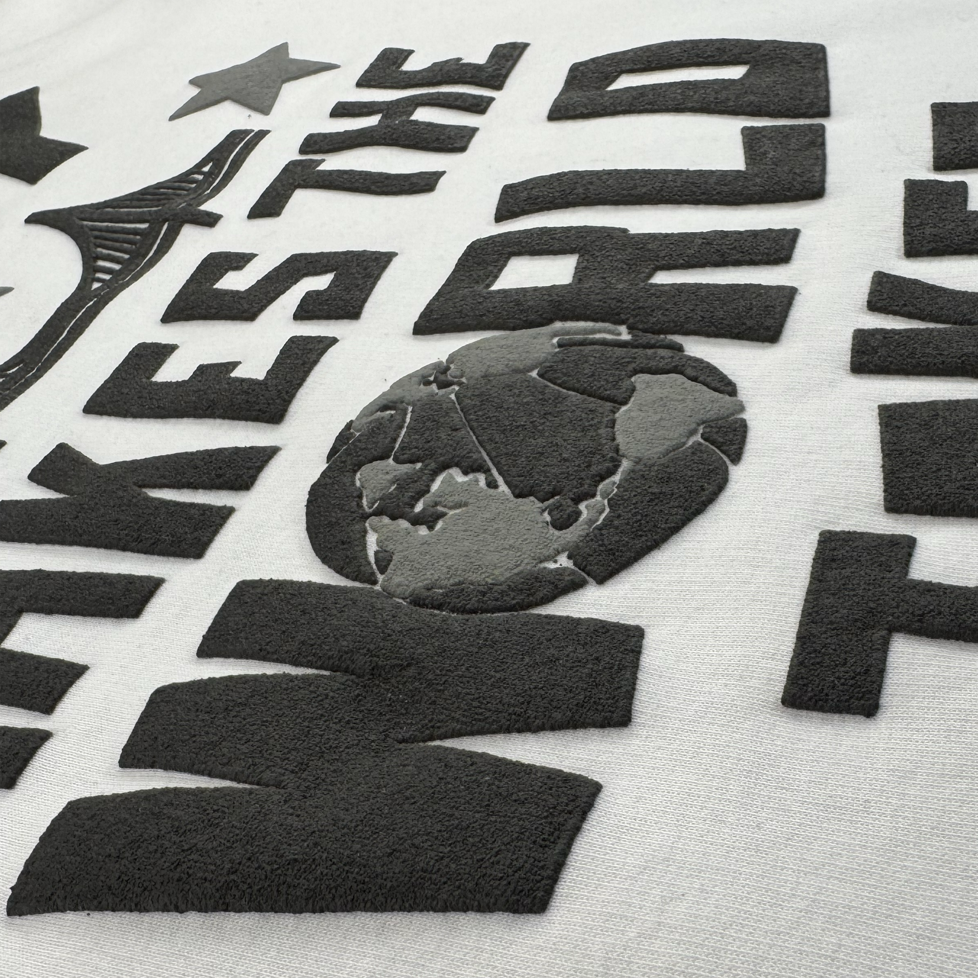 Raised black textured letters and a globe motif add dimension to the Bay Bridge Hoodie By DOC V2 from Oaklandish. Large, bold letters with a soft felt feel appear with a partial star and curved shape on light grey fleece.