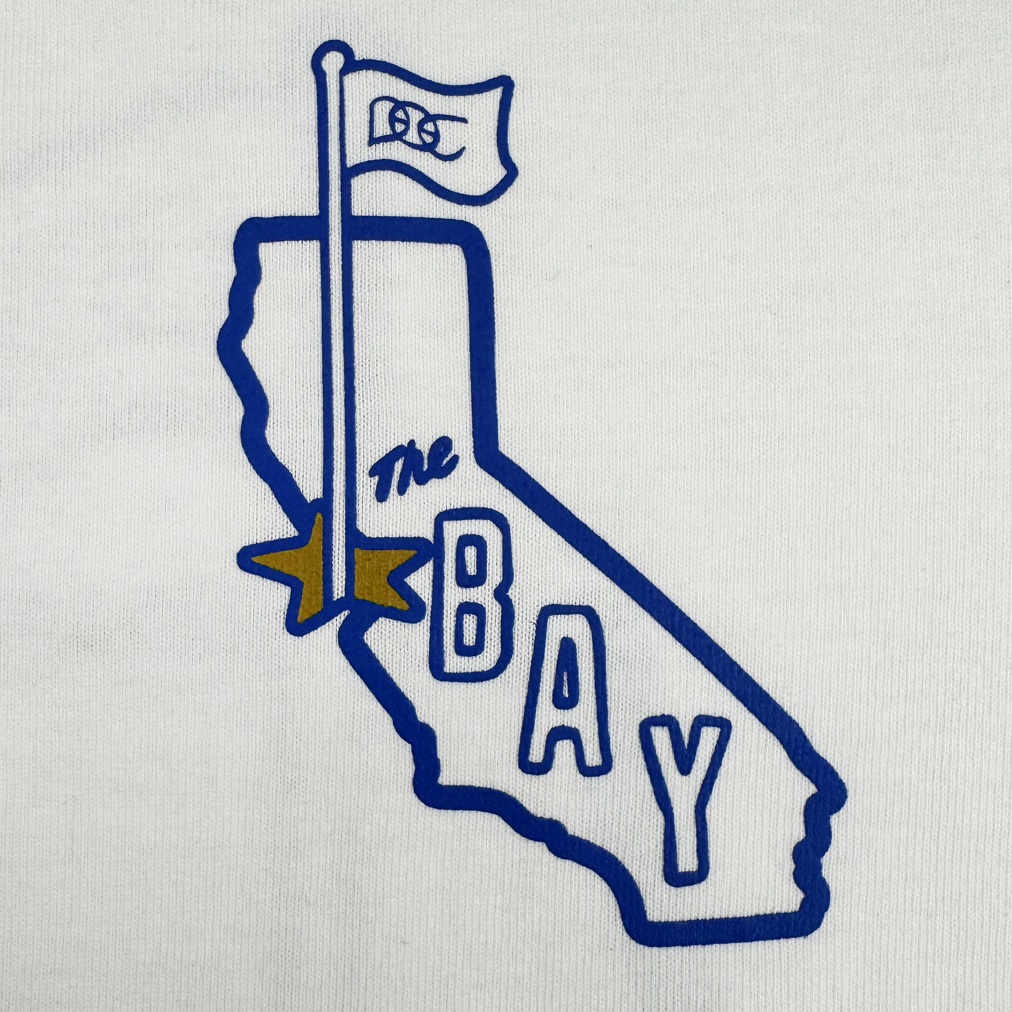 A blue California outline on white with a GSW flag, yellow Bay Area star, and "The BAY" text—featured on the heavyweight CA Bay Area Tee By DOC from Oaklandish.