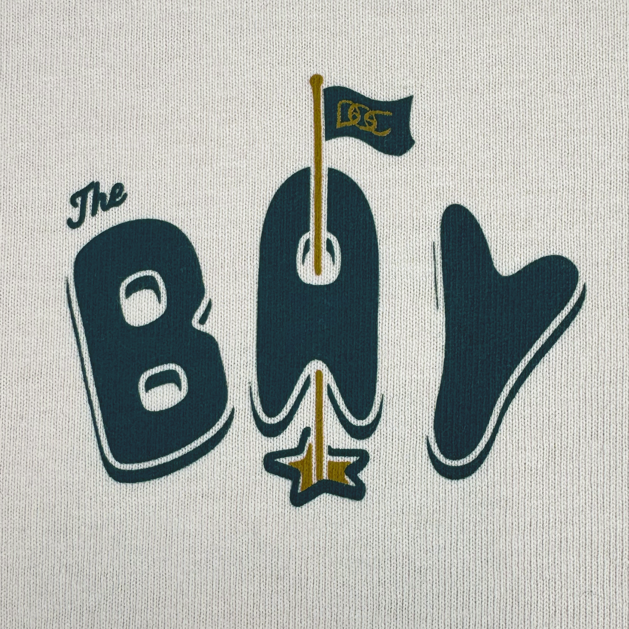 The Bay Flag Tee By DOC by Oaklandish features “The Bay” in bold on heavyweight cotton, with a flagpole “A” topped by a black "BSC" flag and gold star, blending nautical flair and playful style. Part of The Bay Collection.