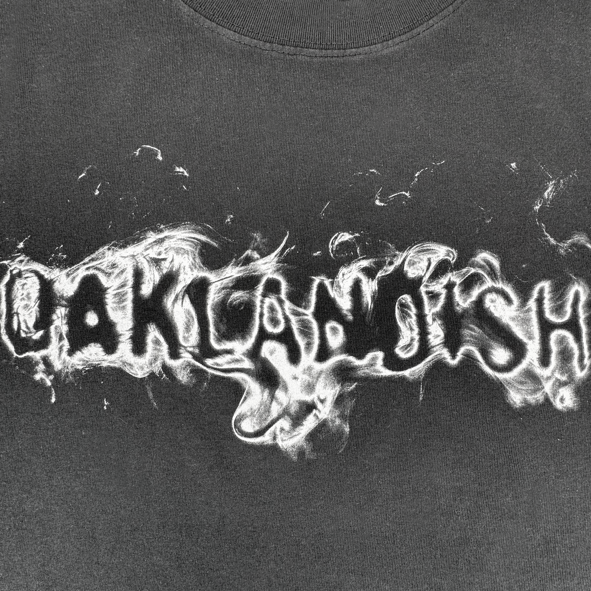 The Oaklandish Haze Tee features a black and white “OAKLANDISH” design in a smoky font drifting across a men’s classic fit black t-shirt, evoking wisps of smoke or flame on heavyweight cotton.