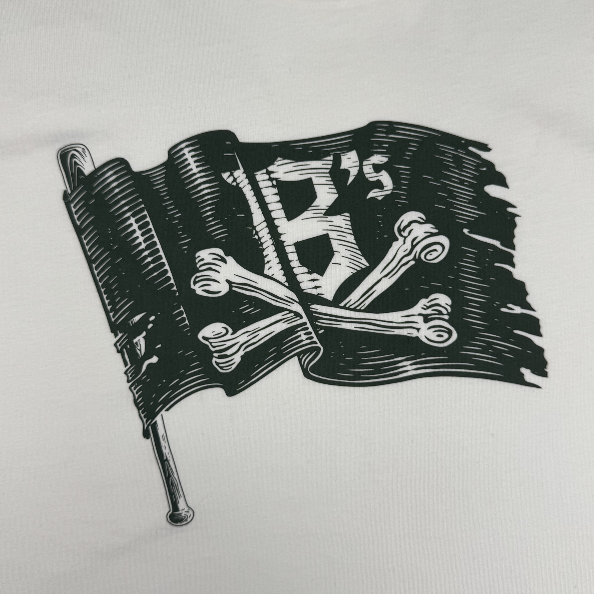 The Jolly Roger Tee by Oakland Ballers features a black pirate flag with white crossbones and a bold "B's" logo, waving on a pole against a plain white background—perfect for fans of the professional baseball team.