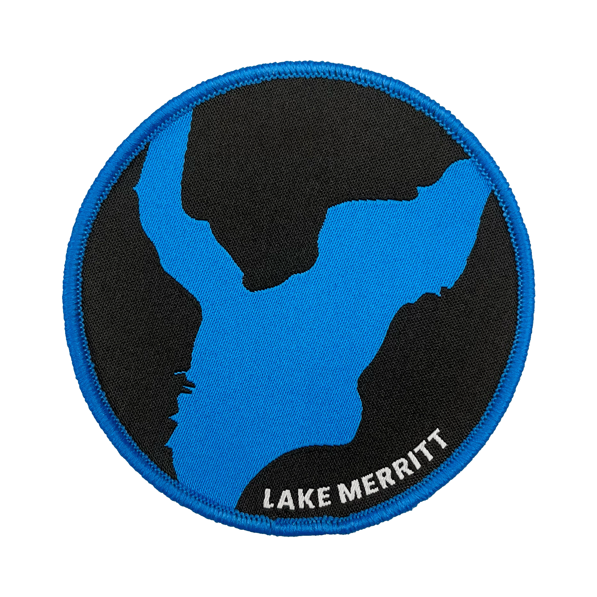 The Oaklandish Lake Merritt Patch is a circular embroidered iron-on patch that features a stylized map outline of Lake Merritt in blue against a black background, with a blue border. The label "LAKE MERRITT" is embroidered in white at the bottom right edge, making it the perfect customized patch for your accessories.