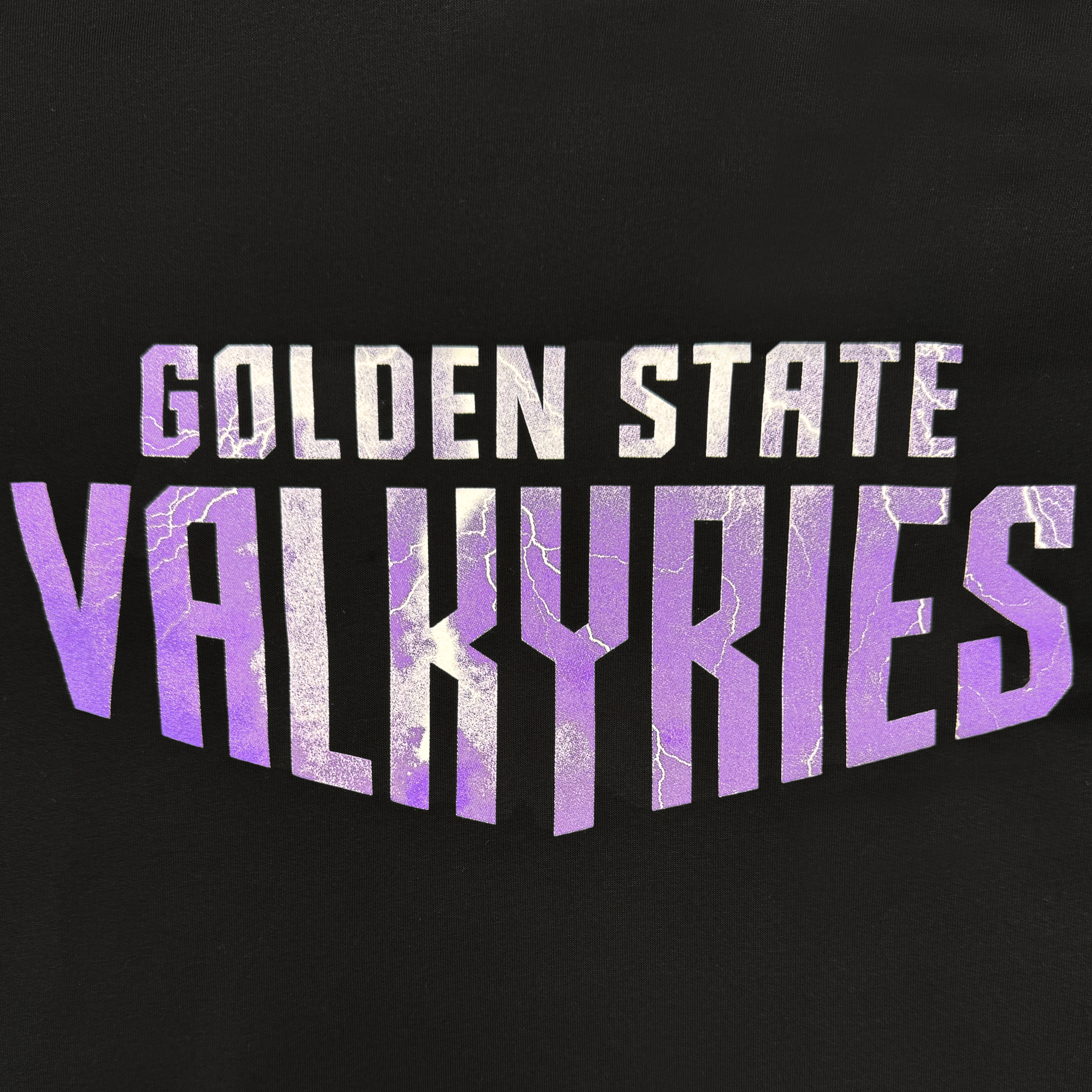 The GSV Golden State Valkyries Violet Lightning Hoodie features bold white "GOLDEN STATE" text above large purple "VALKYRIES" letters with a cracked lightning effect, all centered on black in an angular, crest-like officially licensed design.