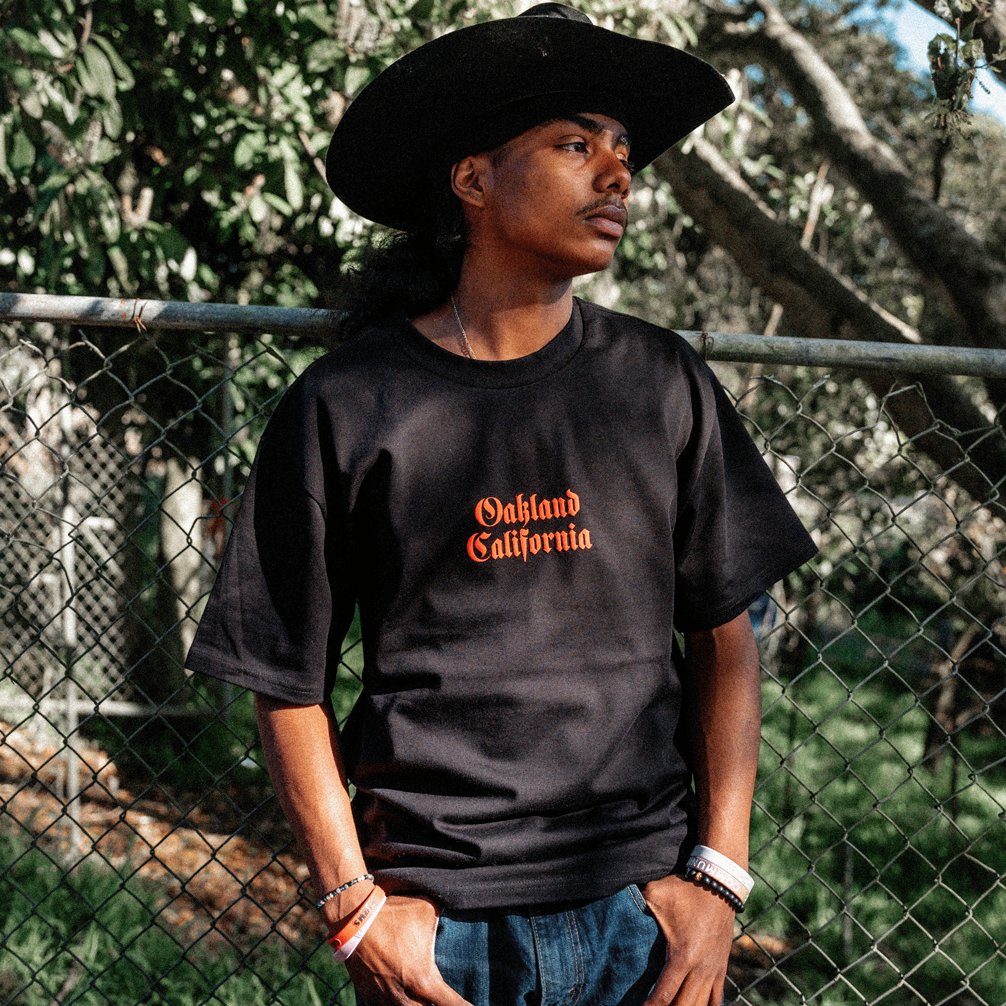 Front view of model outside wearing black tee with Oakland California printed centered in red ink .