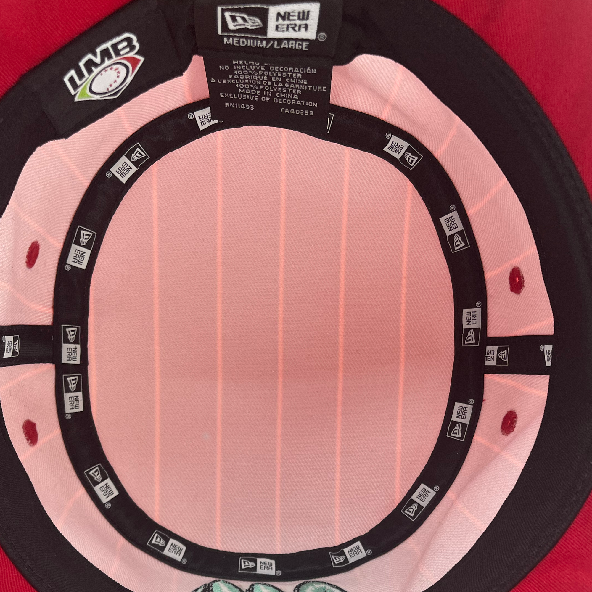 The inside of a red New Era Diablos Paisley Bucket hat is shown. The polyester lining includes size labels indicating "Medium/Large" and various brand tags. A logo with "LMB" and a baseball motif is visible on the inner band. The hat exhibits a pink lining and black trimming around the edge, brought to you by Retail Vendors.