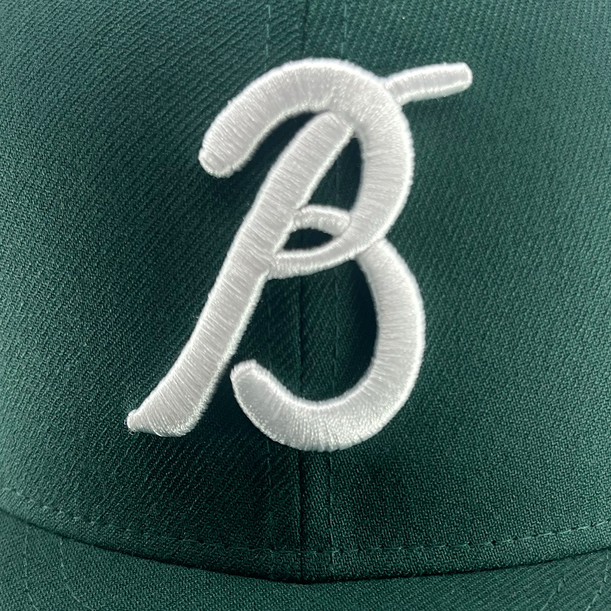 Detailed view of forest green 59fifty fitted hat with Los Bravos logo and new era flag on the left wear side.