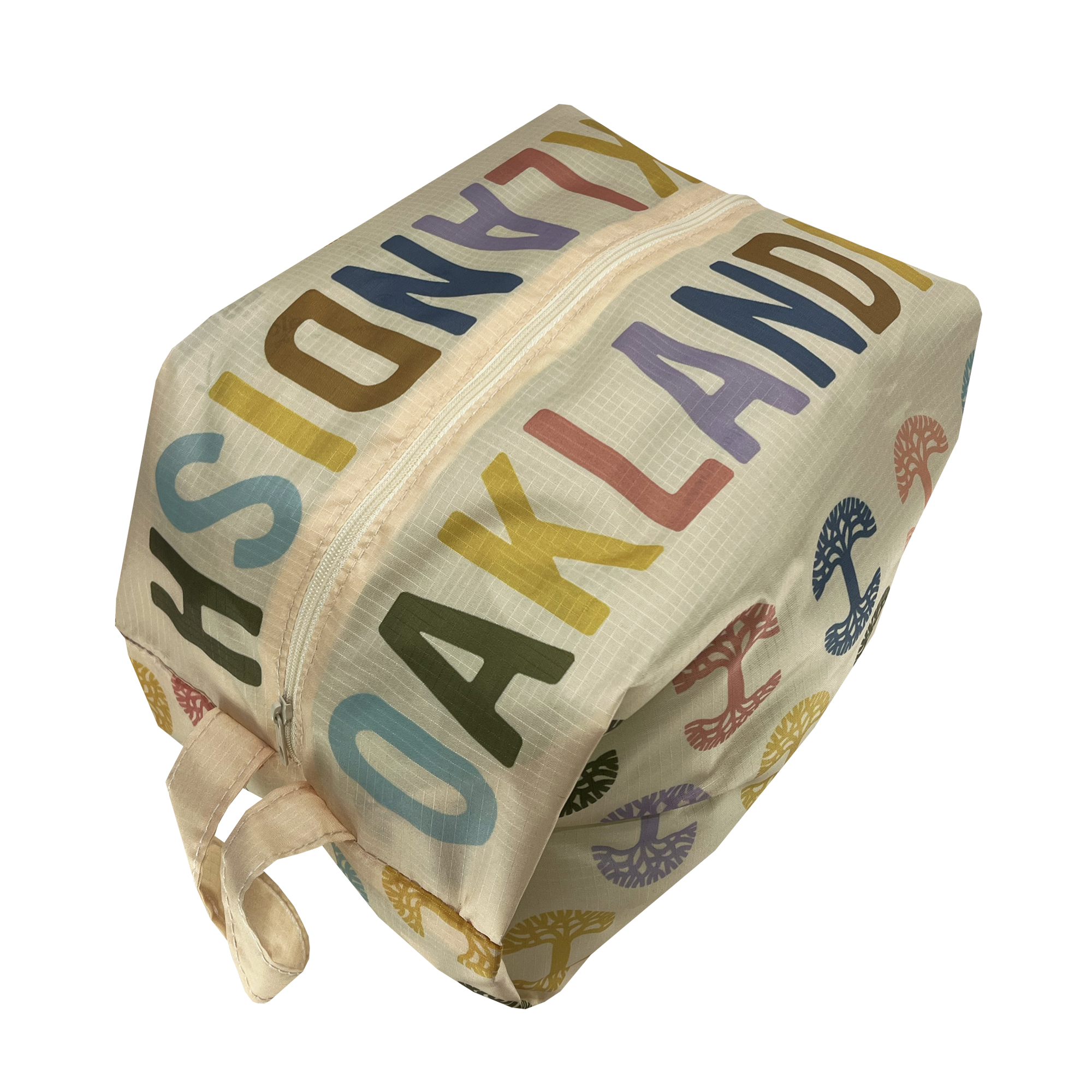 The Oaklandish Repeat Tree Pouch Large - Natural is shown. This durable beige-colored ripstop fabric pouch features a zipper and multicolored text that reads "OAKLANDISH" in varying orientations. It also showcases small tree-like symbols in blue, red, and yellow, with a small handle attached to one end of the pouch.