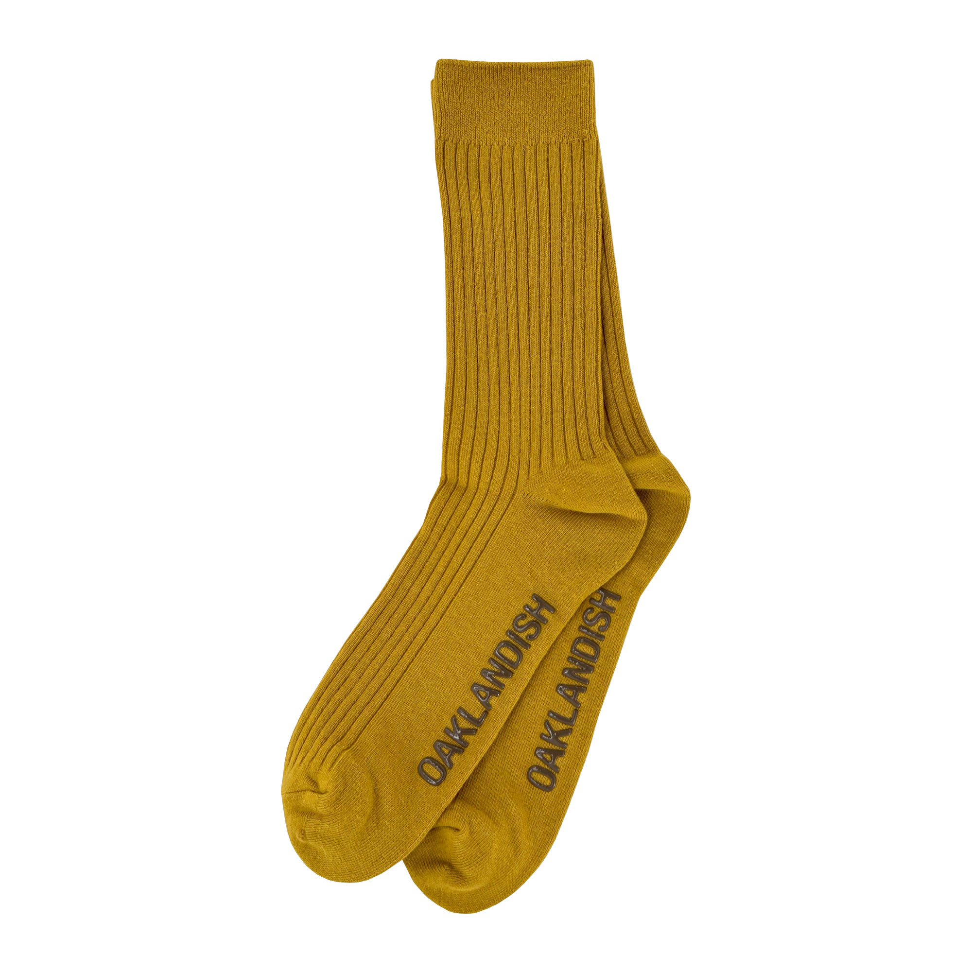 A pair of mustard yellow Grip Crew Socks by Oaklandish, featuring "OAKLANDISH" in dark gray capital letters along the sides. These yellow accessories have a ribbed texture from top to ankle, with reinforced toe and heel areas slightly darker than the rest. They are made from a cotton polyester spandex blend.