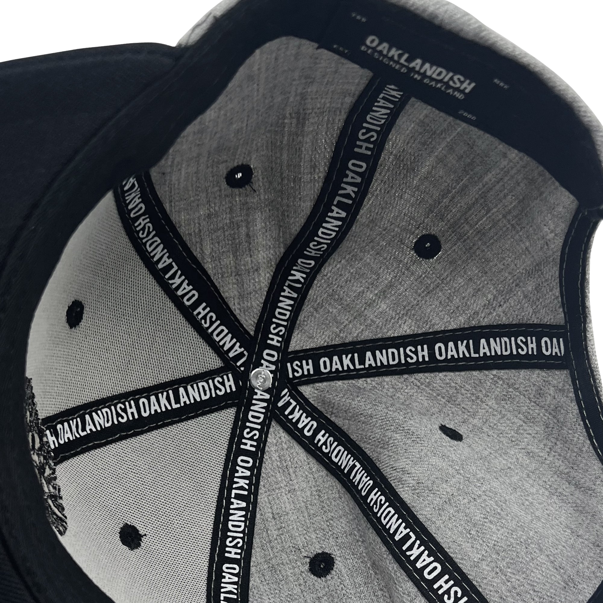 A close-up view of the Oaklandish Classic Snapback reveals its grey and black design. Labels attached to the inner seams feature the "Oaklandish" brand name in white text on a black background. The cap's interior stitching and structure, including fabric-covered ventilation holes, are clearly visible.