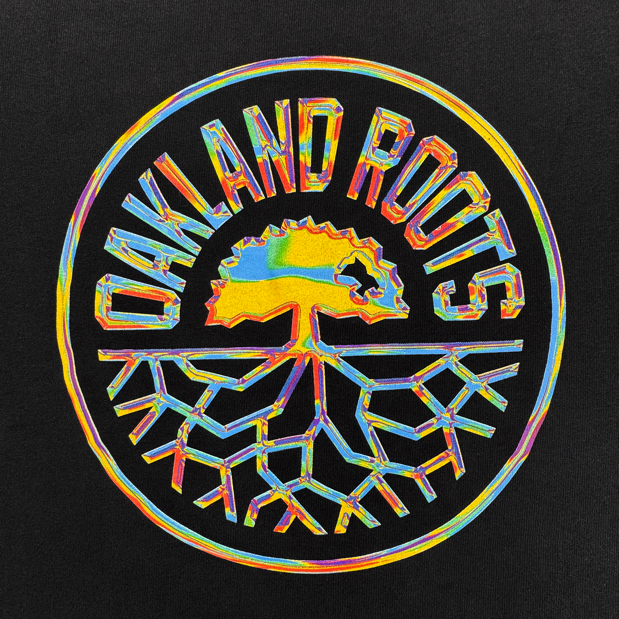 The Iridescent Tee by Oakland Roots SC features a vibrant, psychedelic club logo with a tree and roots in a circle, “OAKLAND ROOTS” above, all on black—a standout Oaklandish design.