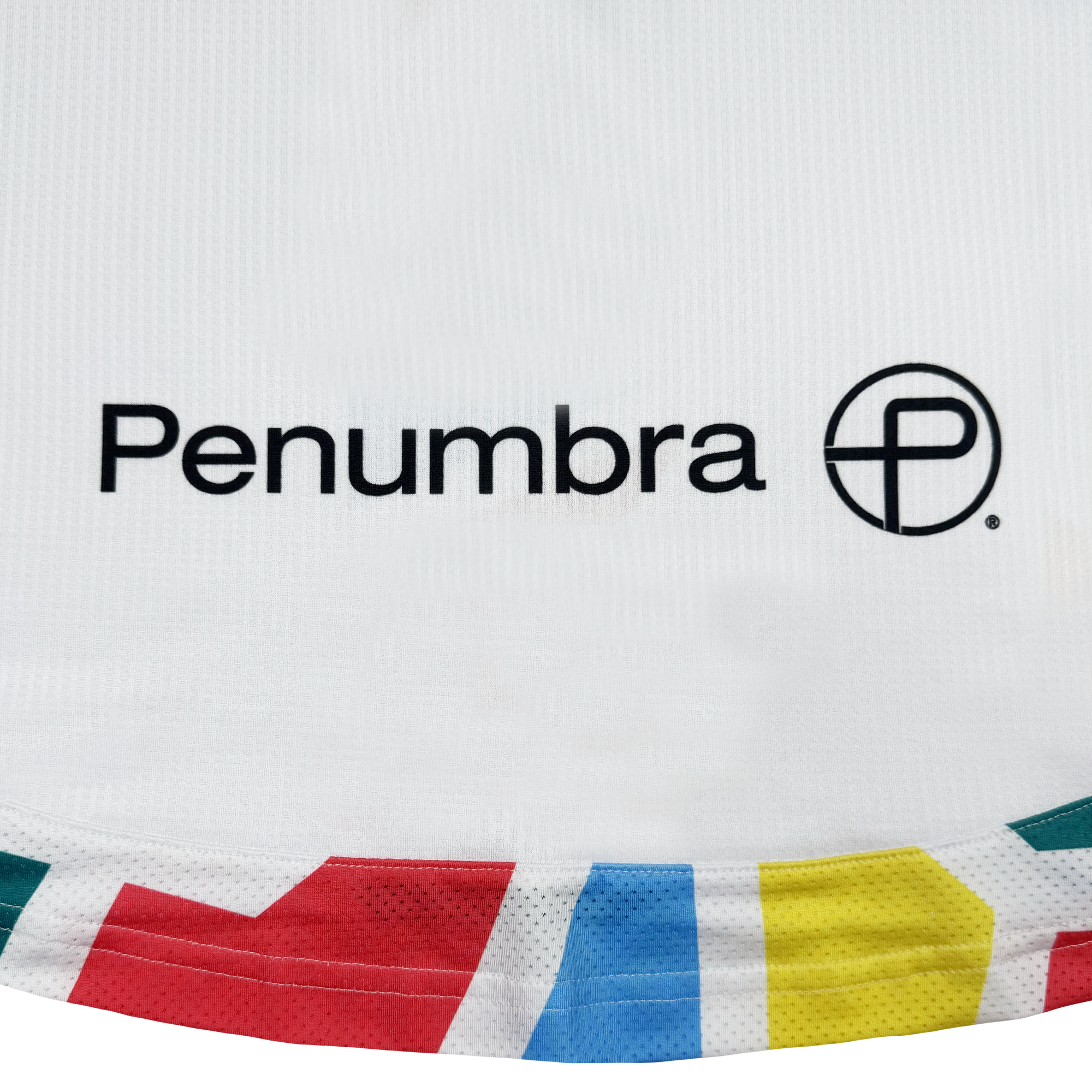 The Unisex Mosaic in Motion Kit by Oakland Roots SC is a white fabric with "Penumbra" and a black circular "P" logo. Its bottom edge features a vibrant red, teal, yellow, and green geometric border—reminiscent of the iconic 2026 kit.