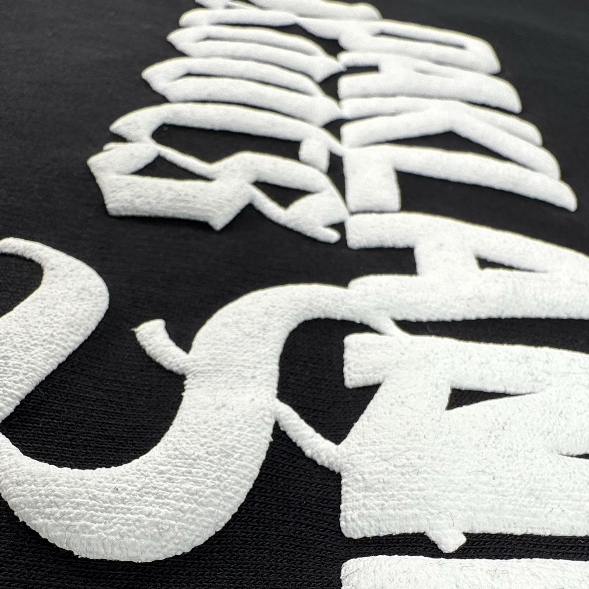 Close-up of bold, raised white embroidery on the black Oakland Roots SC Logo Premium Hoodie by Oakland Roots SC. Textured kanji details add depth and style—ideal for Sports Club or Oakland Roots fans.
