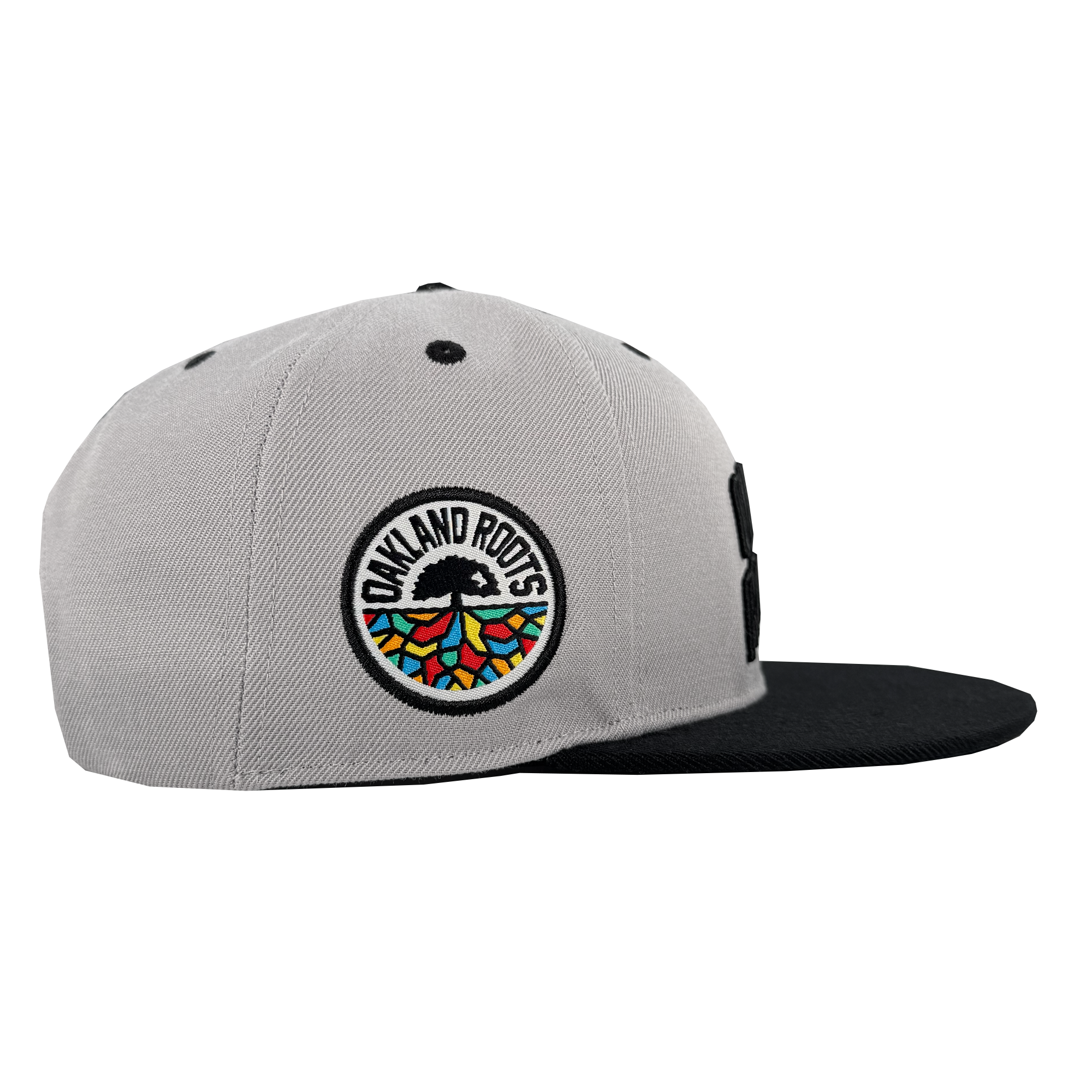 The Oakland Roots SC Arch Text Snapback by Oakland Roots SC is a gray hat with a black brim, featuring a round embroidered Oakland Roots logo with colorful geometric roots and black ventilation eyelets on top.
