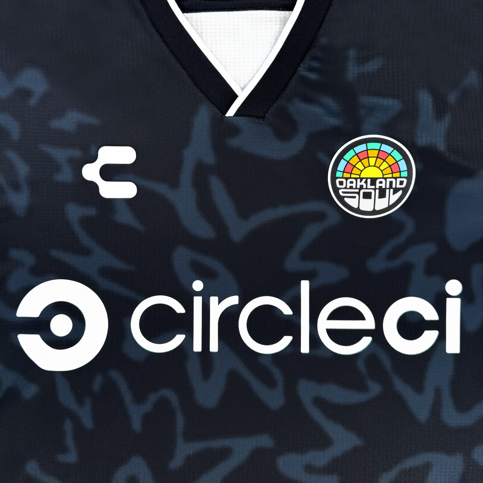 A close-up of the Oakland Soul Unisex Soul Bloom Kit jersey featuring abstract dark patterns, a bold white Circleci logo, a small white E emblem, and a colorful rainbow-motif crest near the collar.