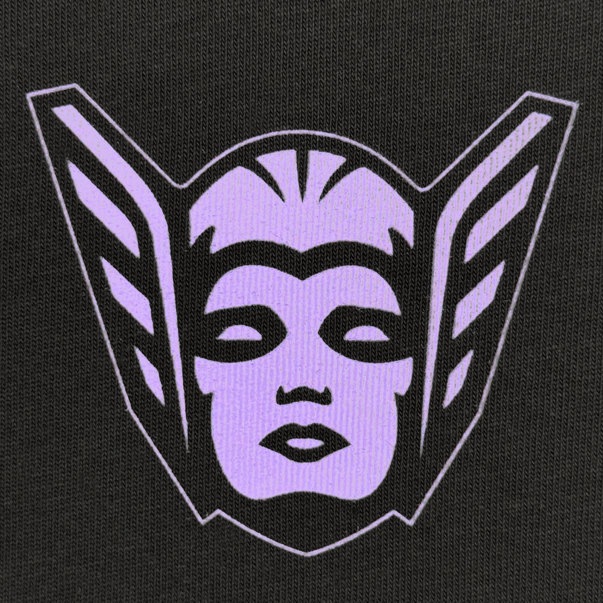 A stylized purple face with closed lips and eyes appears on a black textured background with wing-like shapes, evoking a futuristic helmet—featured on the GSV Golden State Valkyries Renowned Heavy Tee.