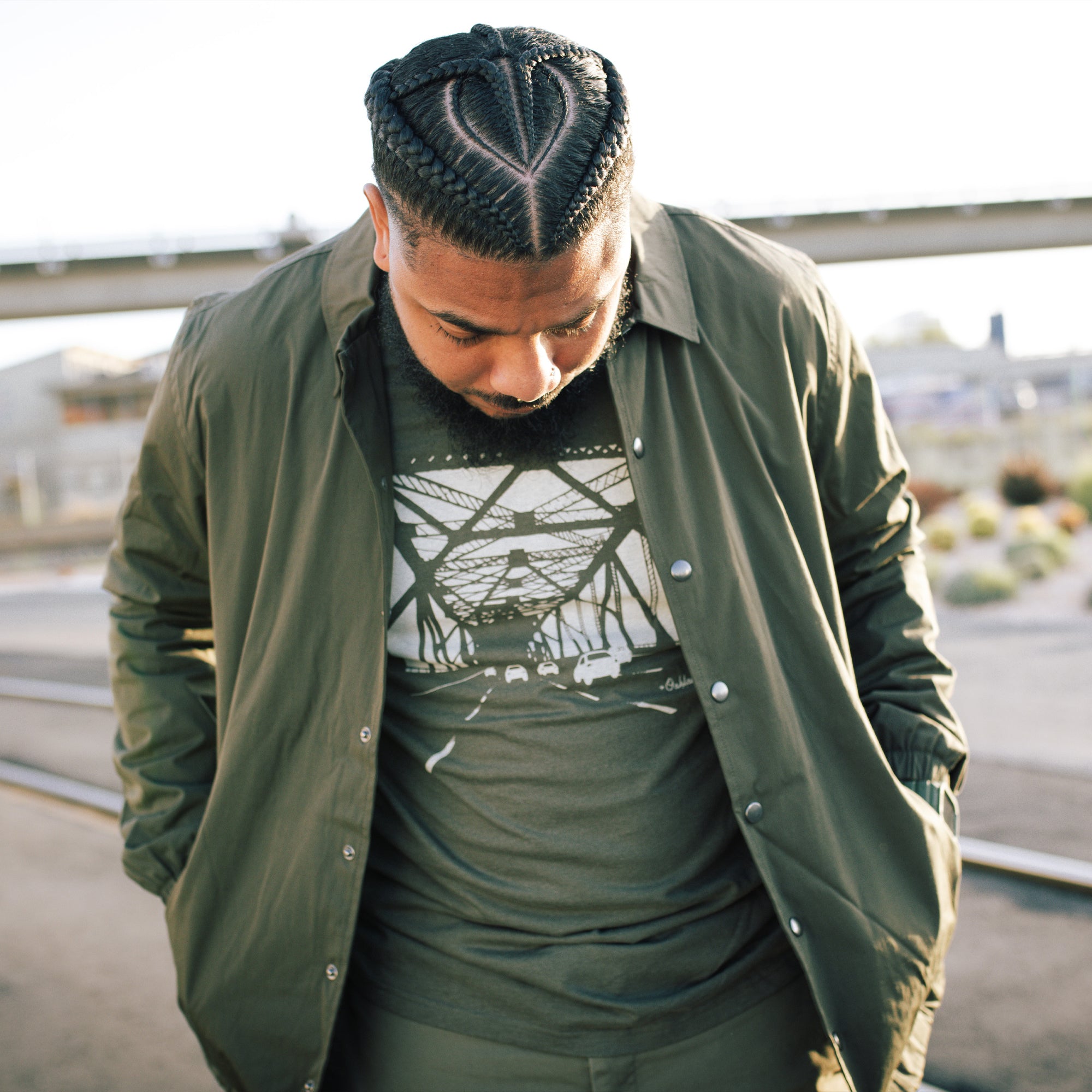 Man in urban area with graffiti in background wearing an open, green cotton, collared, snap close jacket. 