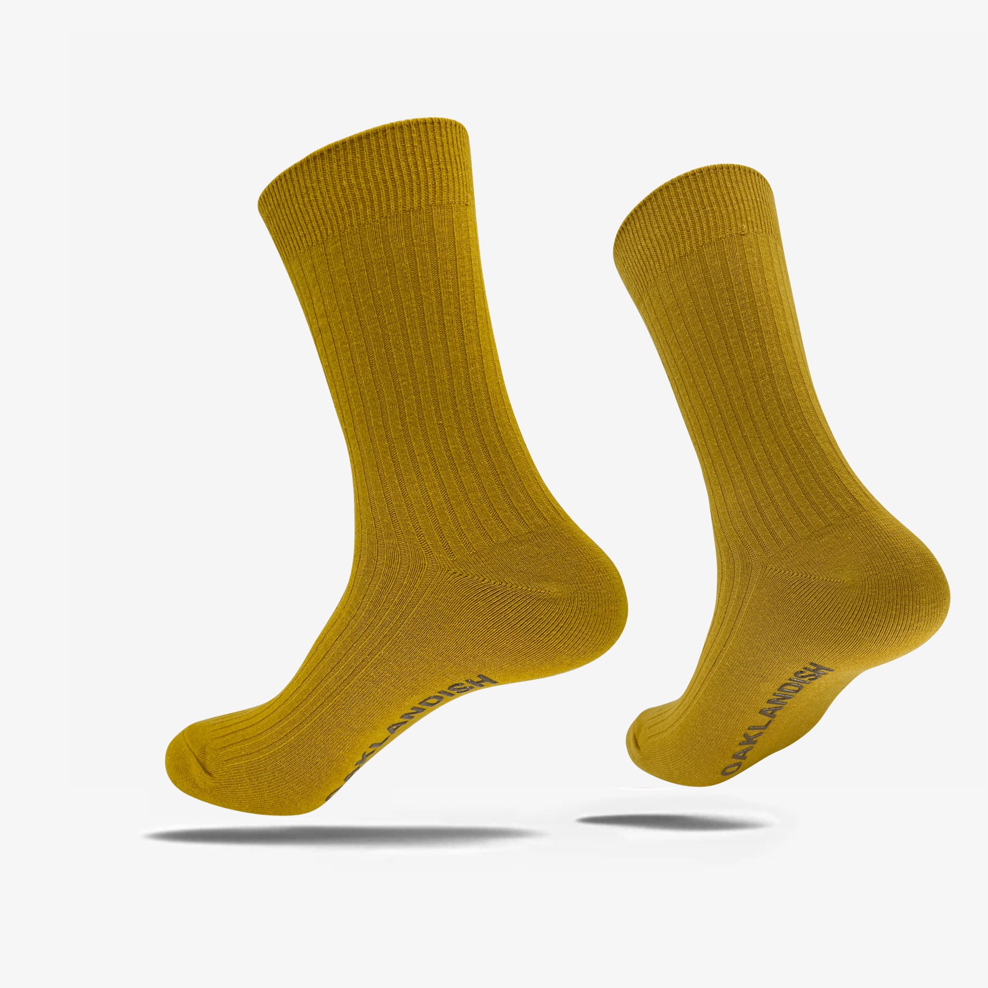 A pair of mustard-yellow Oaklandish Grip Crew Socks are displayed against a plain white background. These cotton polyester spandex socks feature a ribbed texture and mid-calf length, with "SAY HI SOCKS" written on one sole in dark lettering. Both yellow accessories appear to be slightly elevated and angled as if floating.