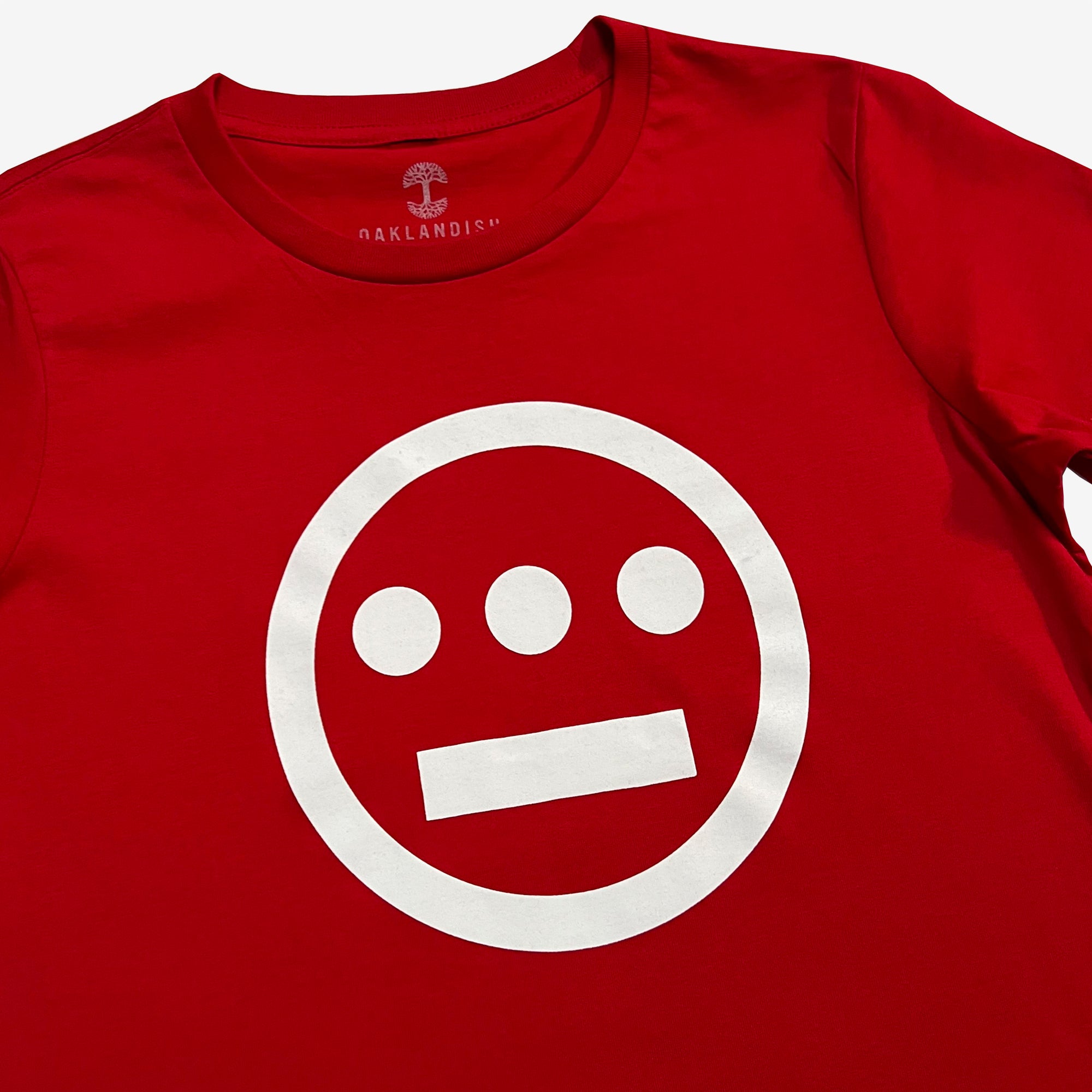 A red Women's Hiero Classic Logo Tee from the brand Hieroglyphics, featuring a white symbol on the front. The design, reminiscent of hieroglyphics, includes a large circle with three smaller filled circles positioned horizontally inside the top portion and a horizontal line inside the bottom portion. Made from 100% cotton, the tag reads "OAKLANDISH.