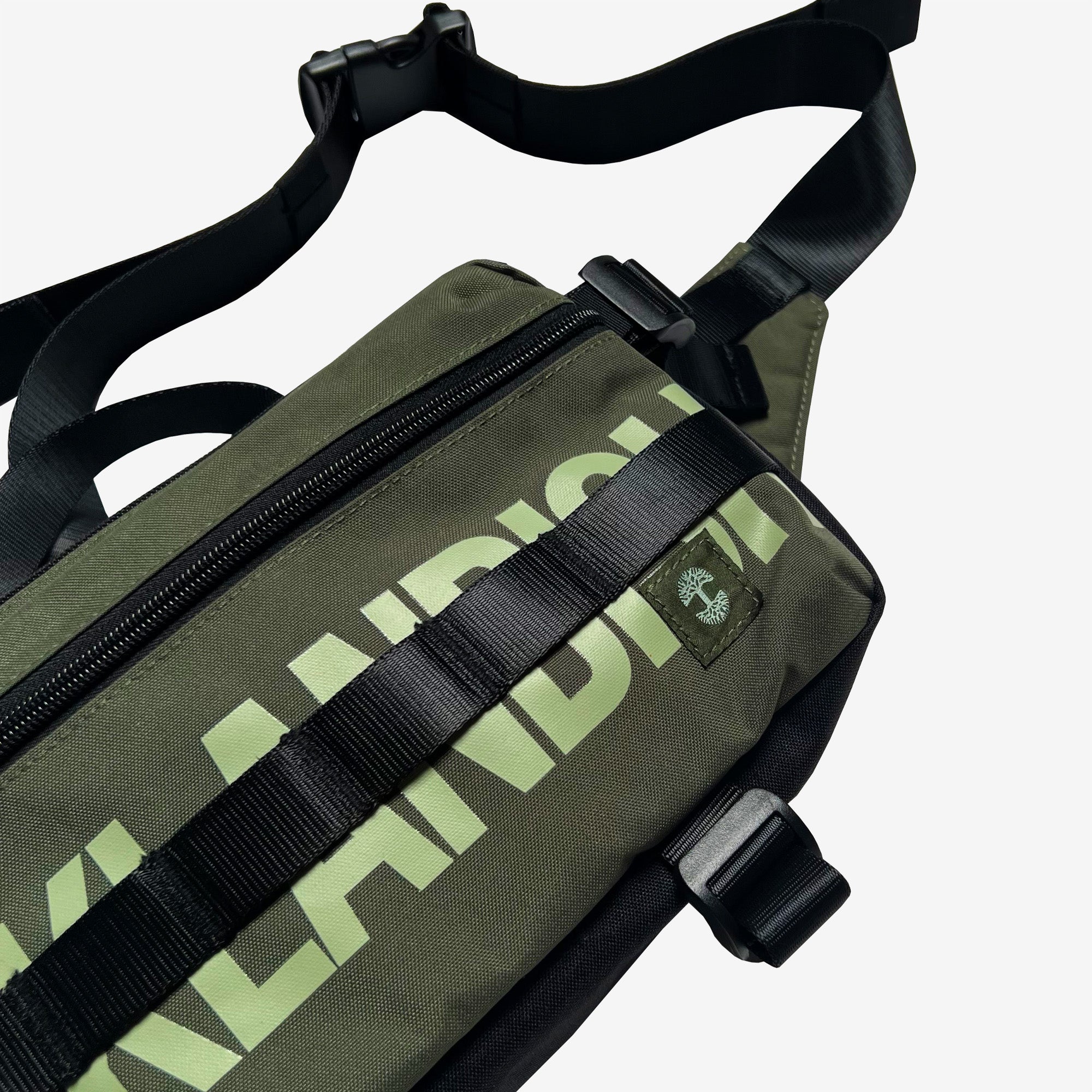 Close up left side olive nylon hip bag with waist belt, & small green Oaklandish tree logo.