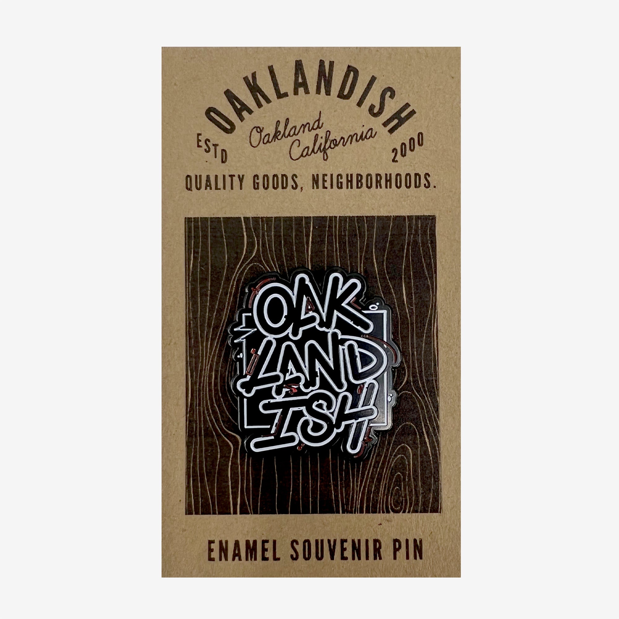 The Enamel Pin - Movement from Oaklandish is featured on a brown cardboard backing. Displaying the word "OAKLANDISH" in a stylized black and white graffiti font, the backing card reads, "OAKLANDISH Estd Oakland California 2000. Quality Goods, Neighborhoods." This accessory is perfect for adding a touch of local pride to any outfit.