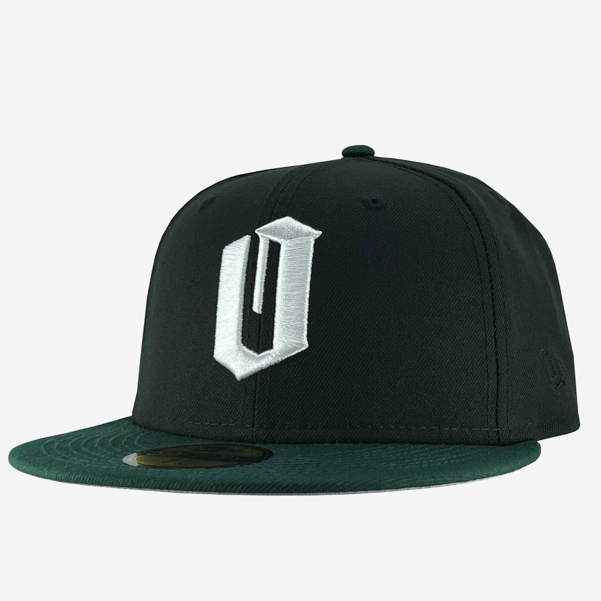 A New Era Official 59FIFTY Fitted Cap by Oaklandish, featuring a black body with a dark green flat brim, displays a large white "U" embroidered in 3D on the front. This clean and minimalistic design is accented by a circular sticker on the brim, indicating it is new or unworn.