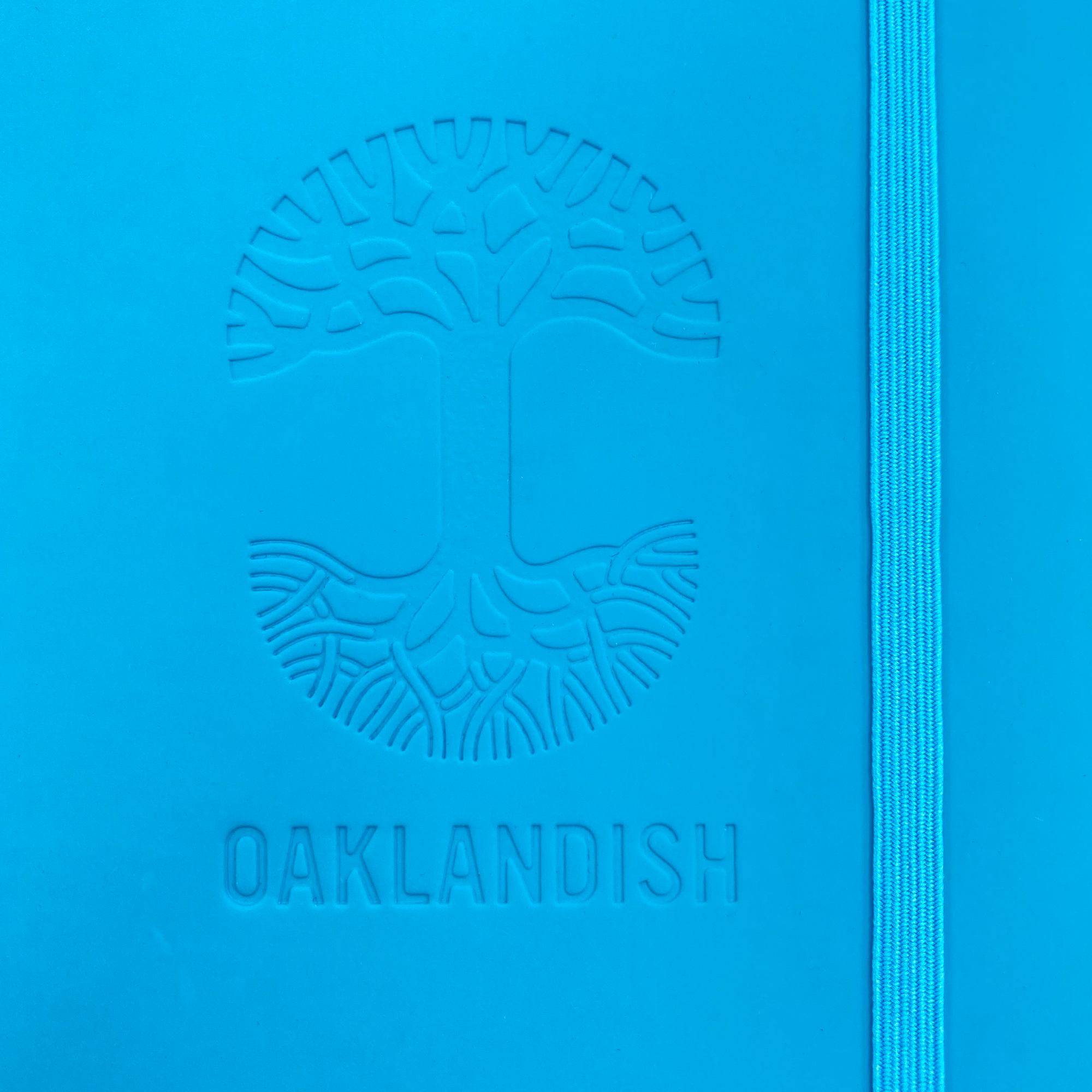 Detailed close-up of embossed Oaklandish tree logo on the front of a blue journal notebook.