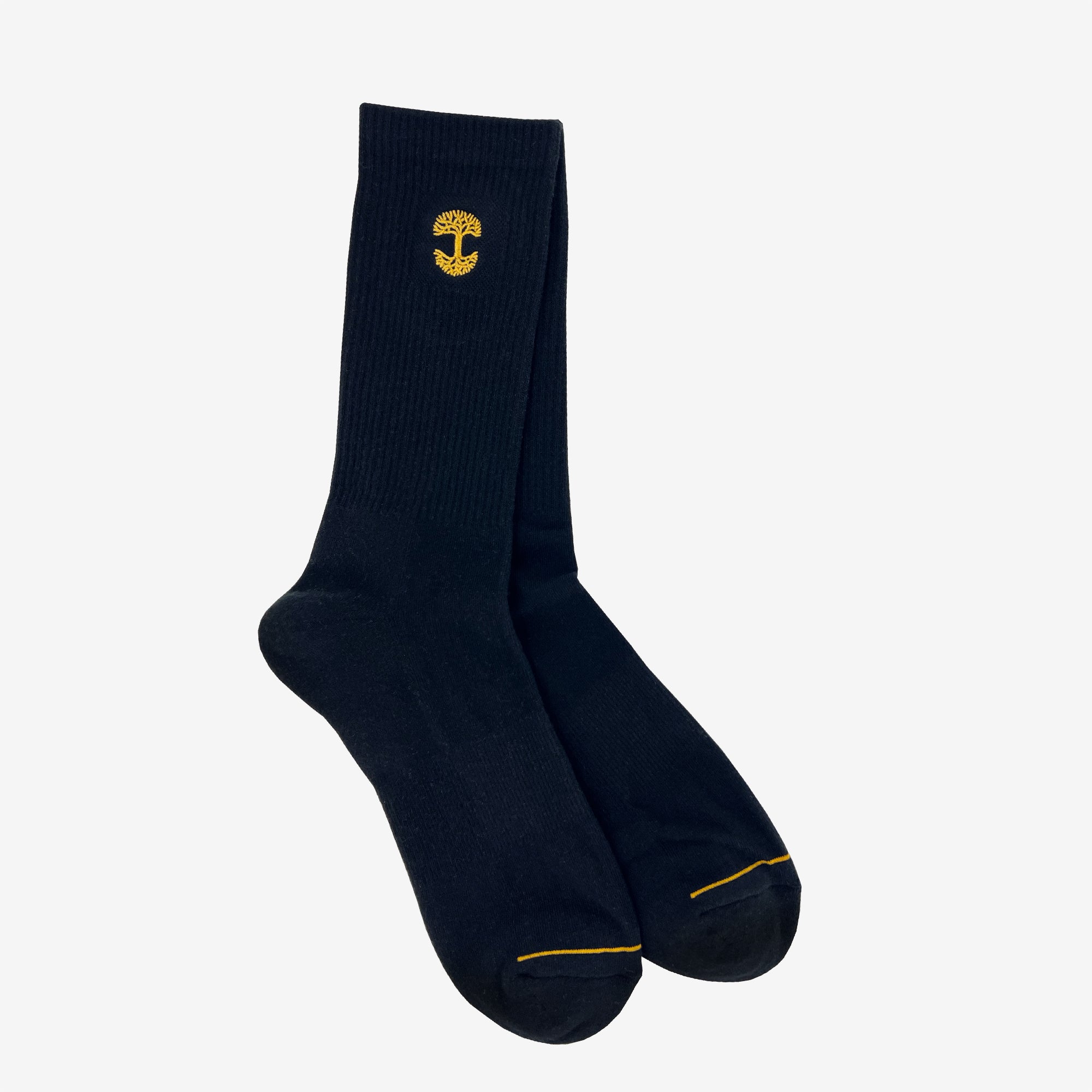 The Embroidered Logo Sock by Oaklandish is a pair of black/gold crew socks, featuring a small yellow mushroom logo embroidered near the top. These adult-sized socks have a ribbed texture on the upper portion and smooth fabric on the foot area, as well as reinforced toes stitched with yellow thread for added durability.