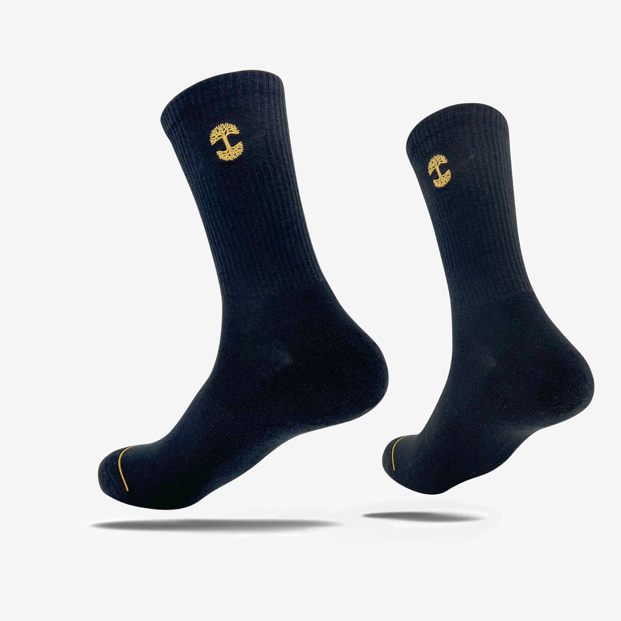 Two Embroidered Logo Socks from Oaklandish, made in a ribbed material with a black and gold color scheme, are shown against a plain white background. These crew socks showcase the iconic yellow Oaklandish logo near the top and a subtle yellow detail near the toe area. They appear to be mid-calf length and are slightly elevated, giving the impression of floating.