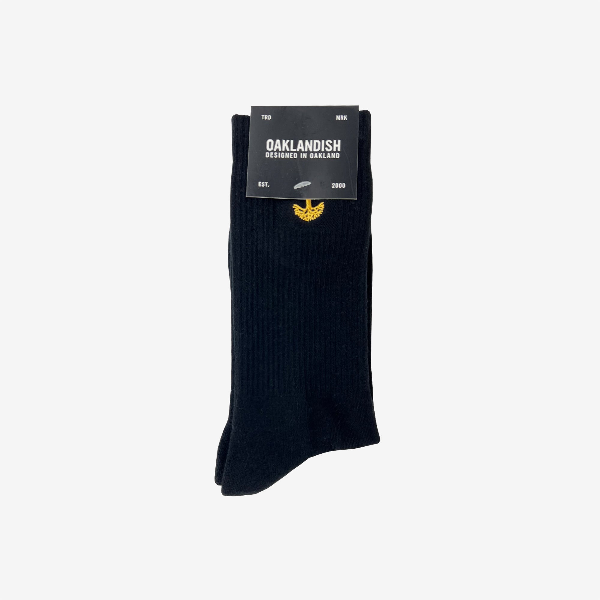 A pair of Oaklandish Embroidered Logo Socks in black/gold, displayed against a white background. The socks feature a small yellow emblem near the top. The packaging reads "OAKLANDISH" and "DESIGNED IN OAKLAND" in white text, along with "EST. 2000" and "MIX." Available in adult sizes.