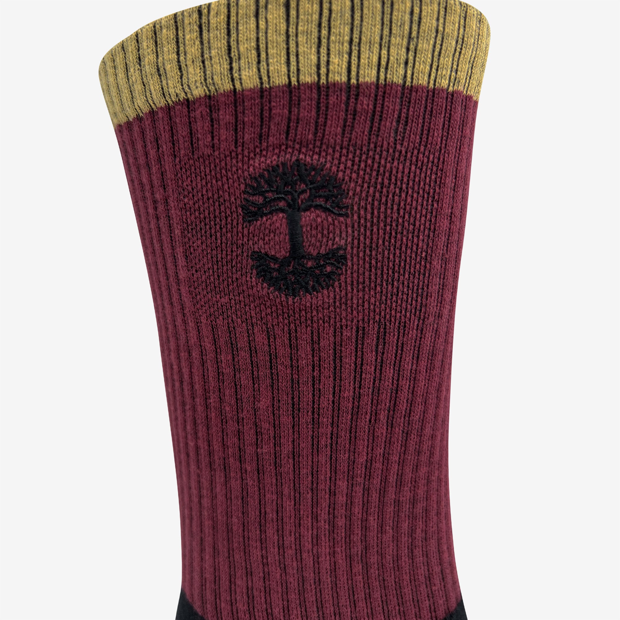 A close-up view of the Colorblock Sock by Oaklandish showcases its upper section, featuring a mustard-yellow band at the top, followed by a wider maroon section with vertical ribbing. An embroidered Oaklandish logo is knitted into the maroon section, and the lower part of the sock is black.