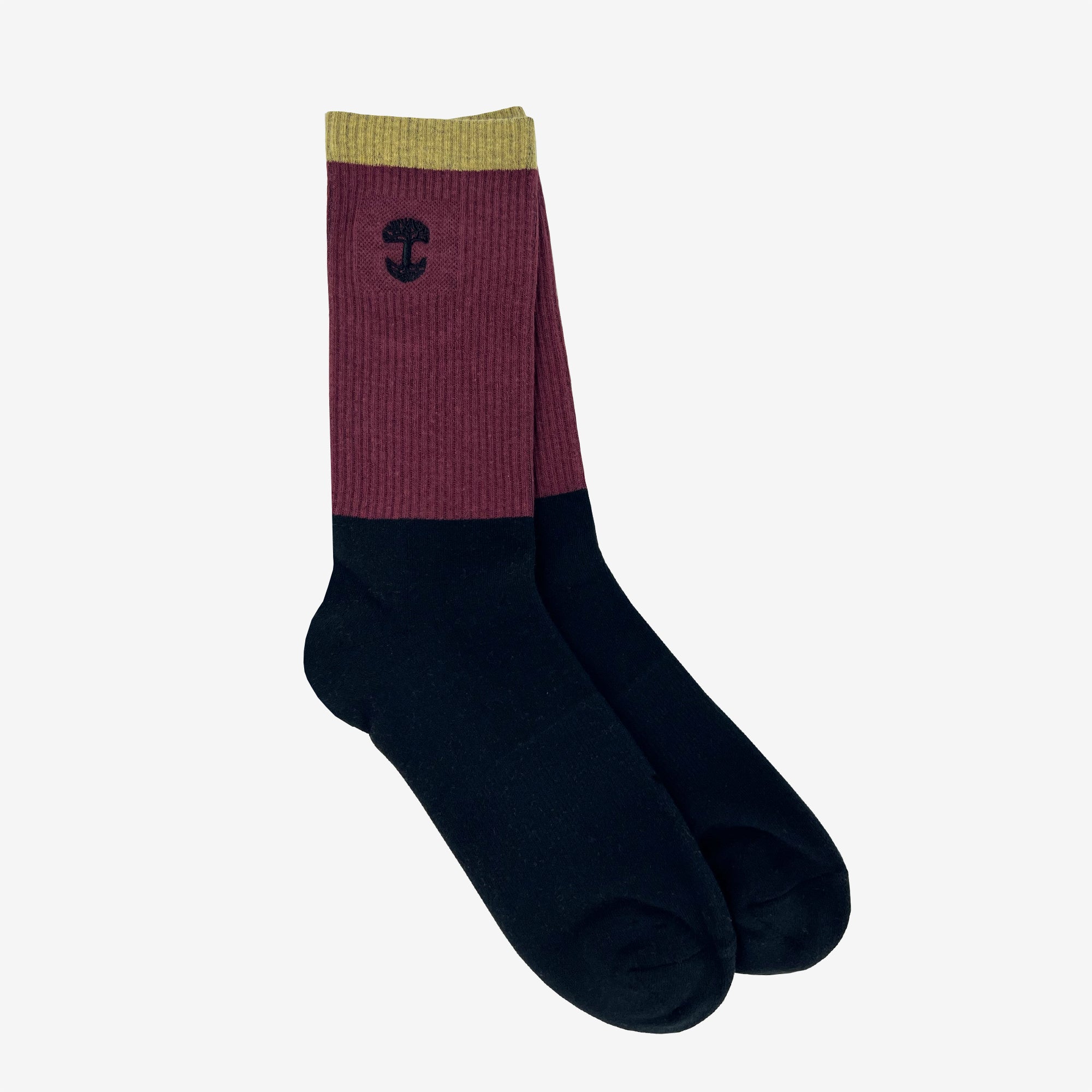 The Oaklandish Colorblock Sock features a unique color block design, with olive green at the top, a maroon middle section, and black covering the lower part. An embroidered Oaklandish logo adorns the maroon portion near the top. The background is plain white.